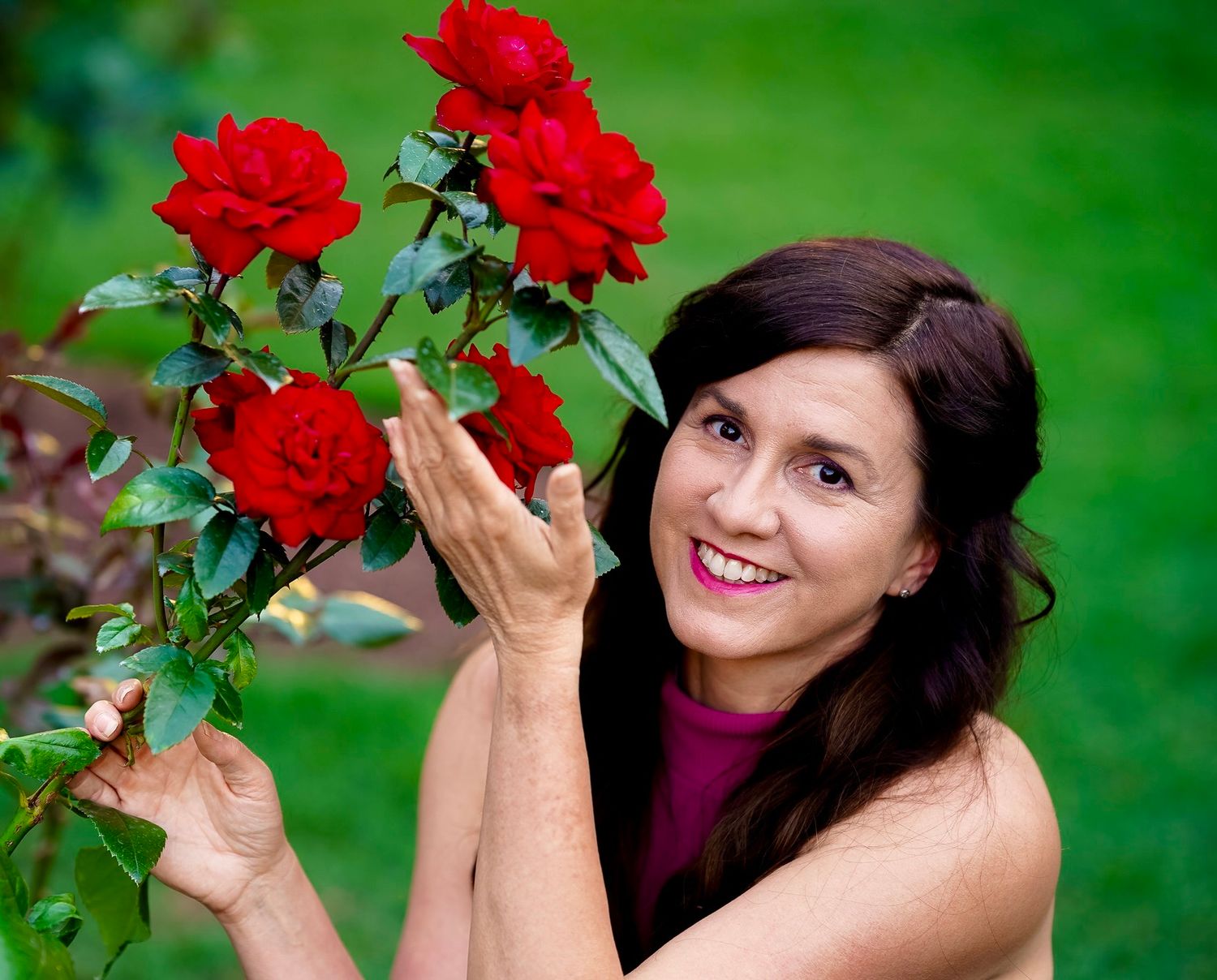 Someone admires vibrant red roses blooming in a garden with a lush green background.