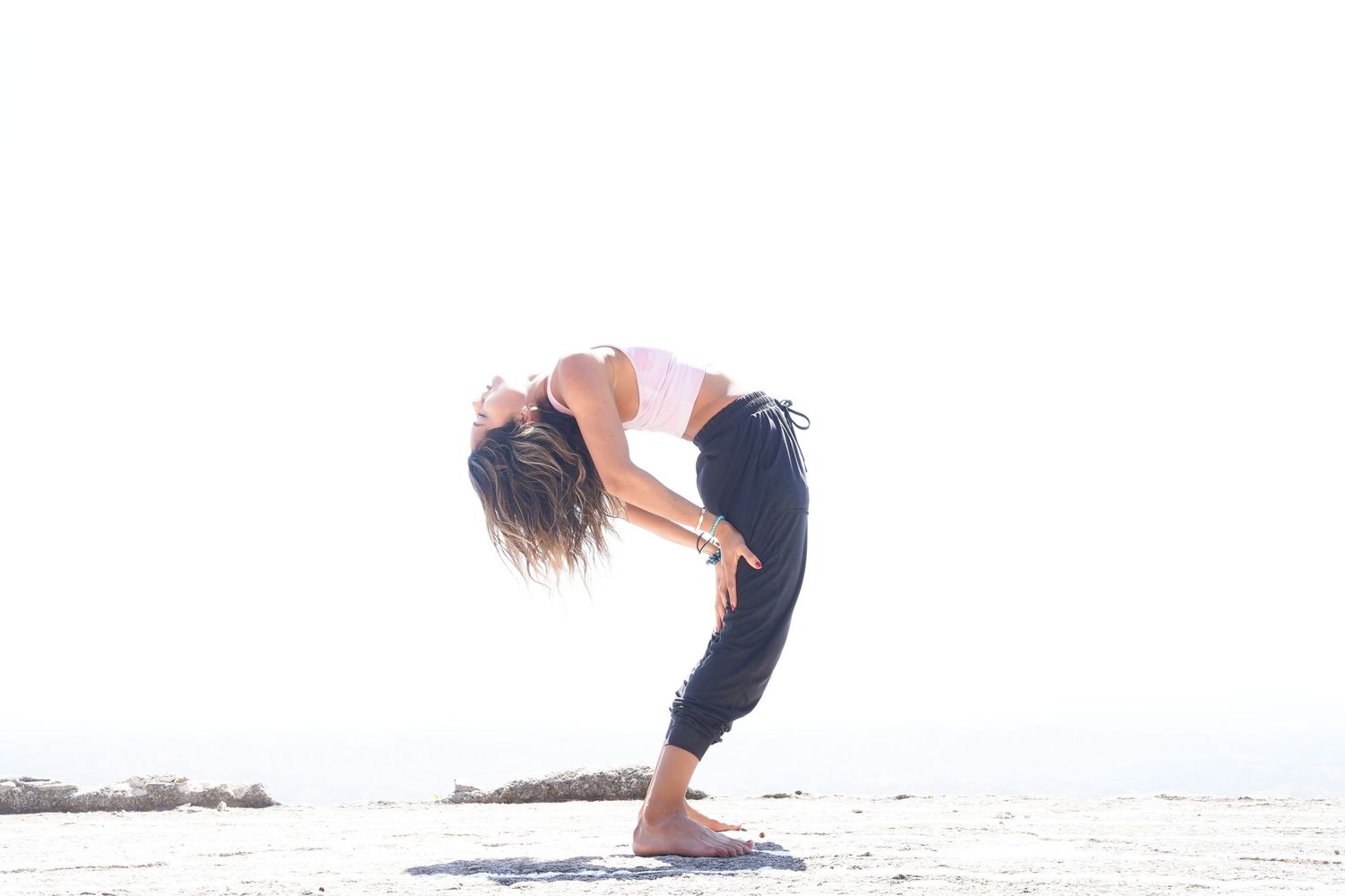 Woman practicing yoga pose outdoors, bending forward with hands on knees on a bright sunny day near the ocean.