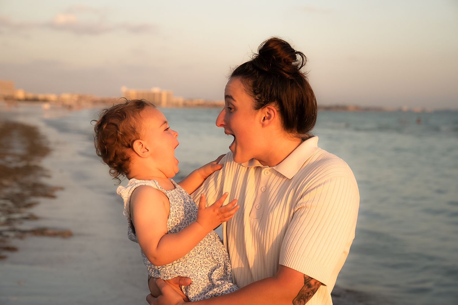 A photo of a mother and daughter laughing at each other with the ocean behind them.