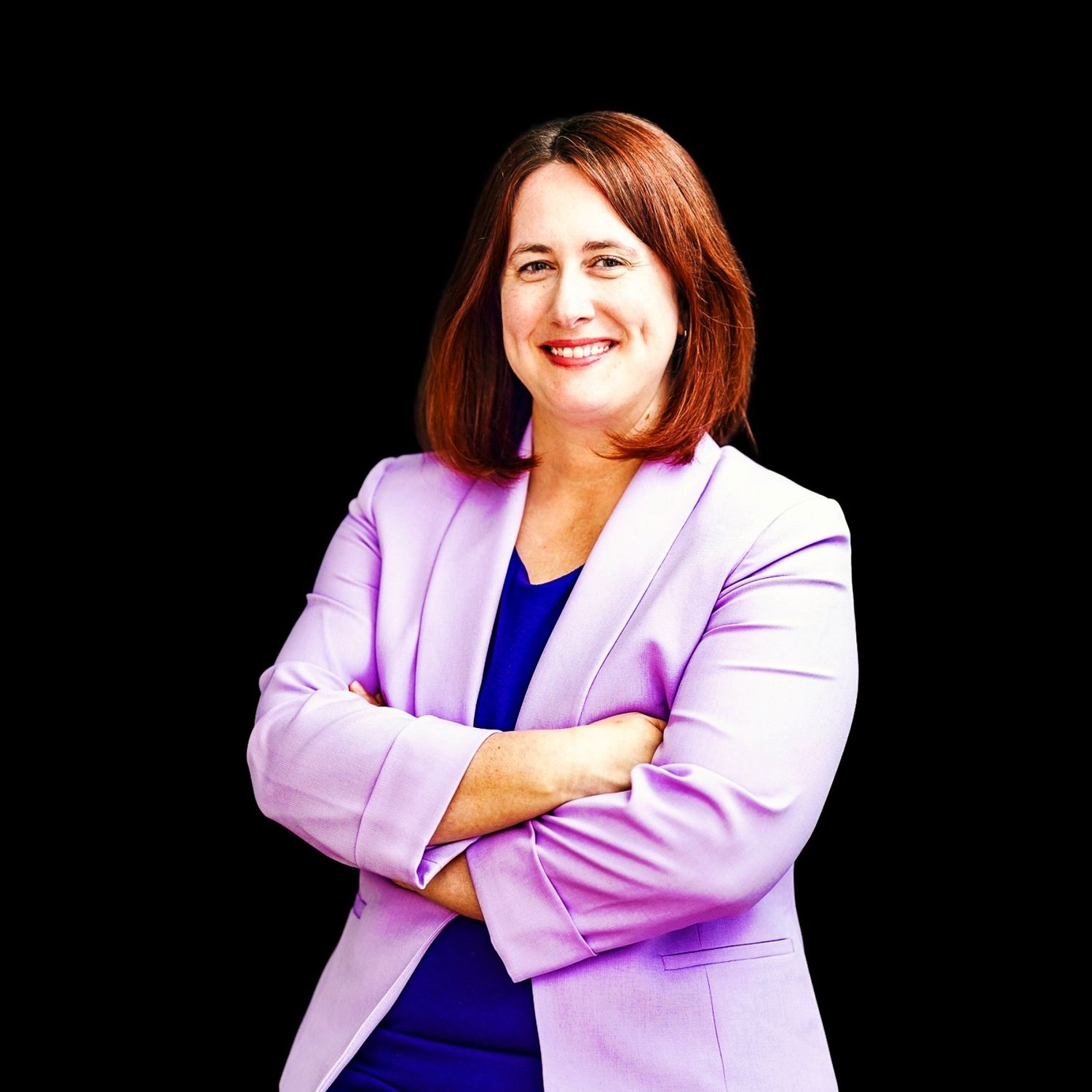 A photo of a woman with her arms crossed wearing a purple jacket with a purple shirt smiling at the camera on a black backdrop.