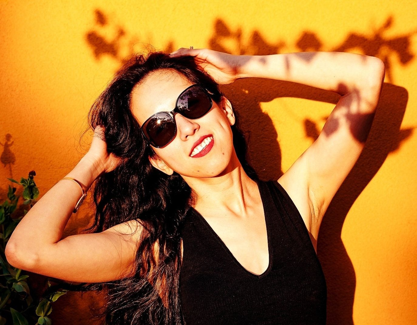 A photo of a woman with black hair wearing a black tank top and red lipstick, black sunglasses.