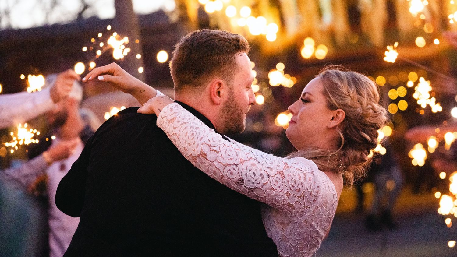 A bride and groom share a romantic first dance surrounded by sparkling lights at their wedding reception.