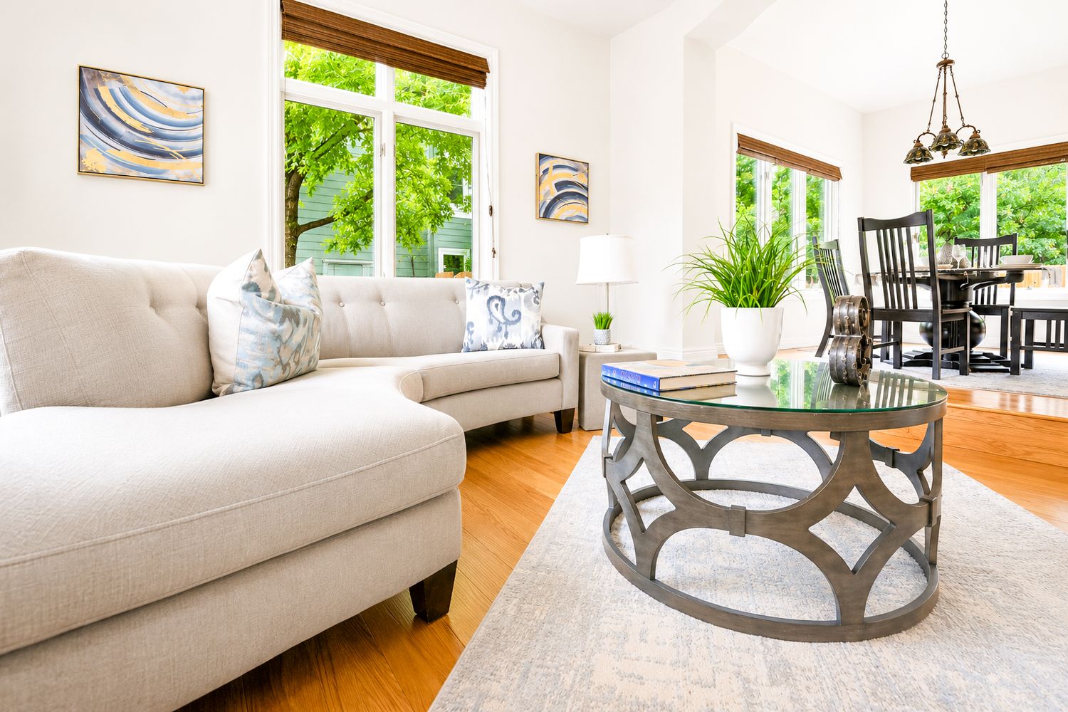 Bright living room with beige sofa, glass coffee table, hardwood floors, and large windows letting in natural light.