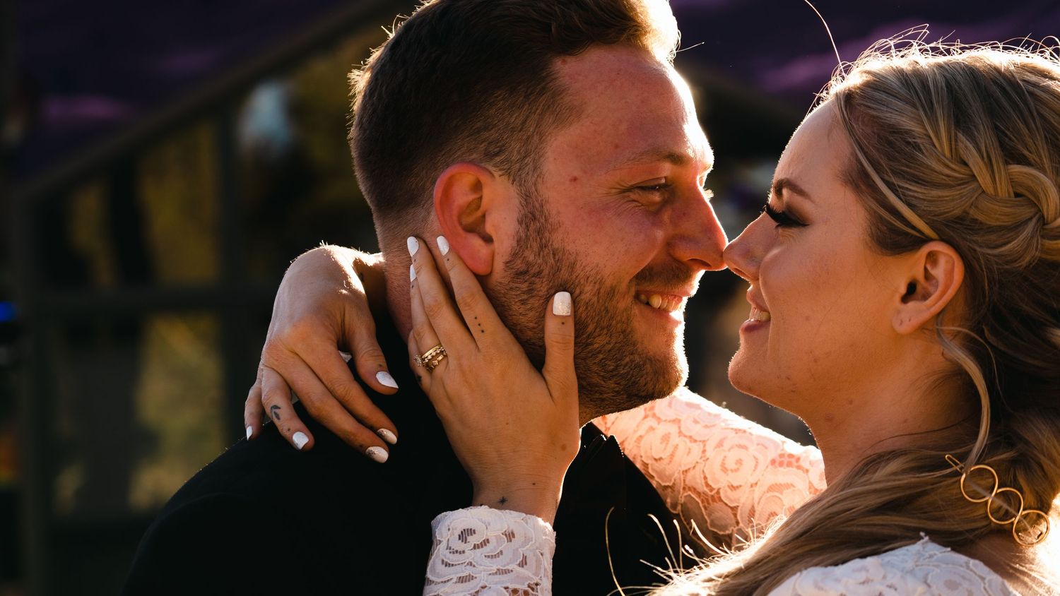A joyful couple shares an intimate moment, the bride wearing a lace dress and diamond ring, bathed in warm golden sunlight.