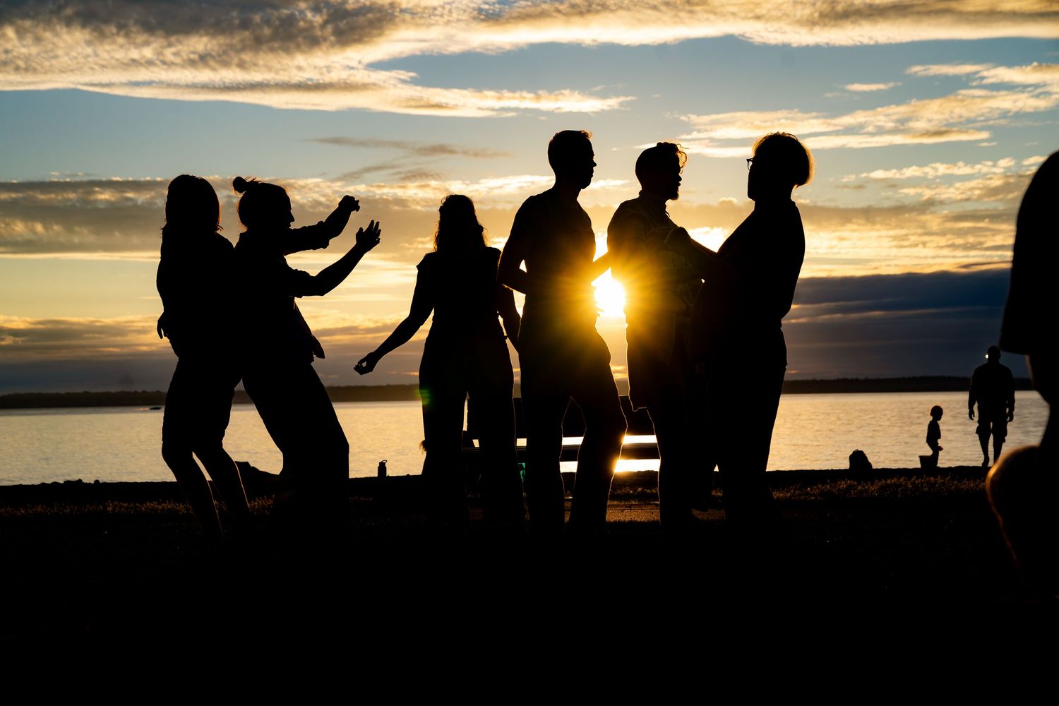 Silhouettes of a group of people socializing on a beach at sunset with golden sky and water in background.