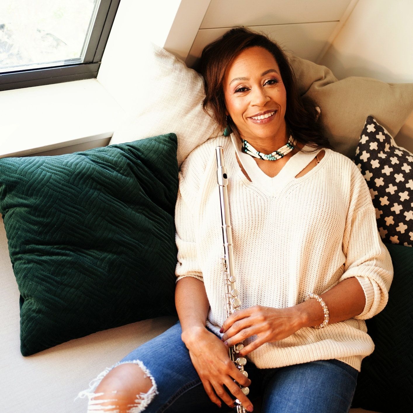 A photo of a woman holding a flute and wearing a tan shirt and blue pants.