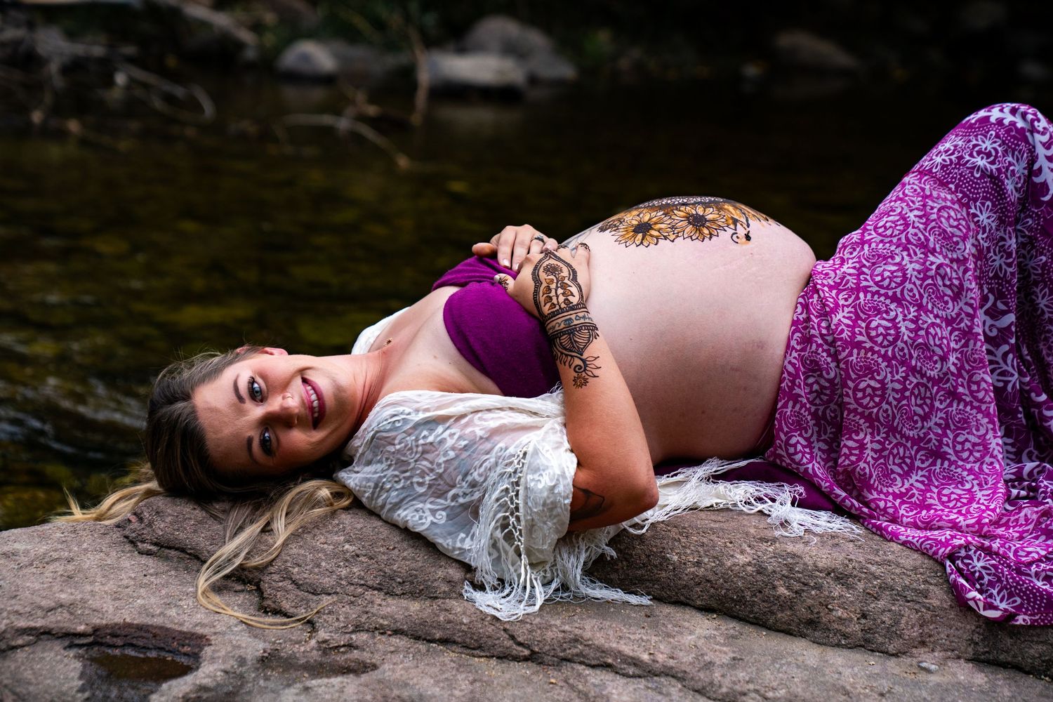 A person in a white top and purple skirt lies artistically posed across rocky terrain in a creative photoshoot.