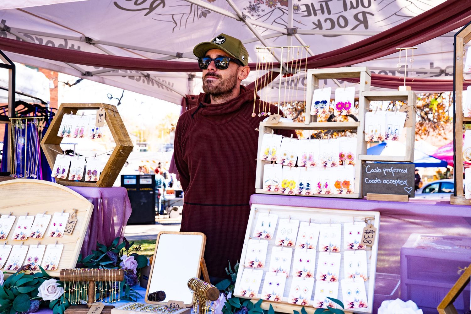 Man smiling at the Hand Pressed Flower Jewelry booth at the farmers market.
