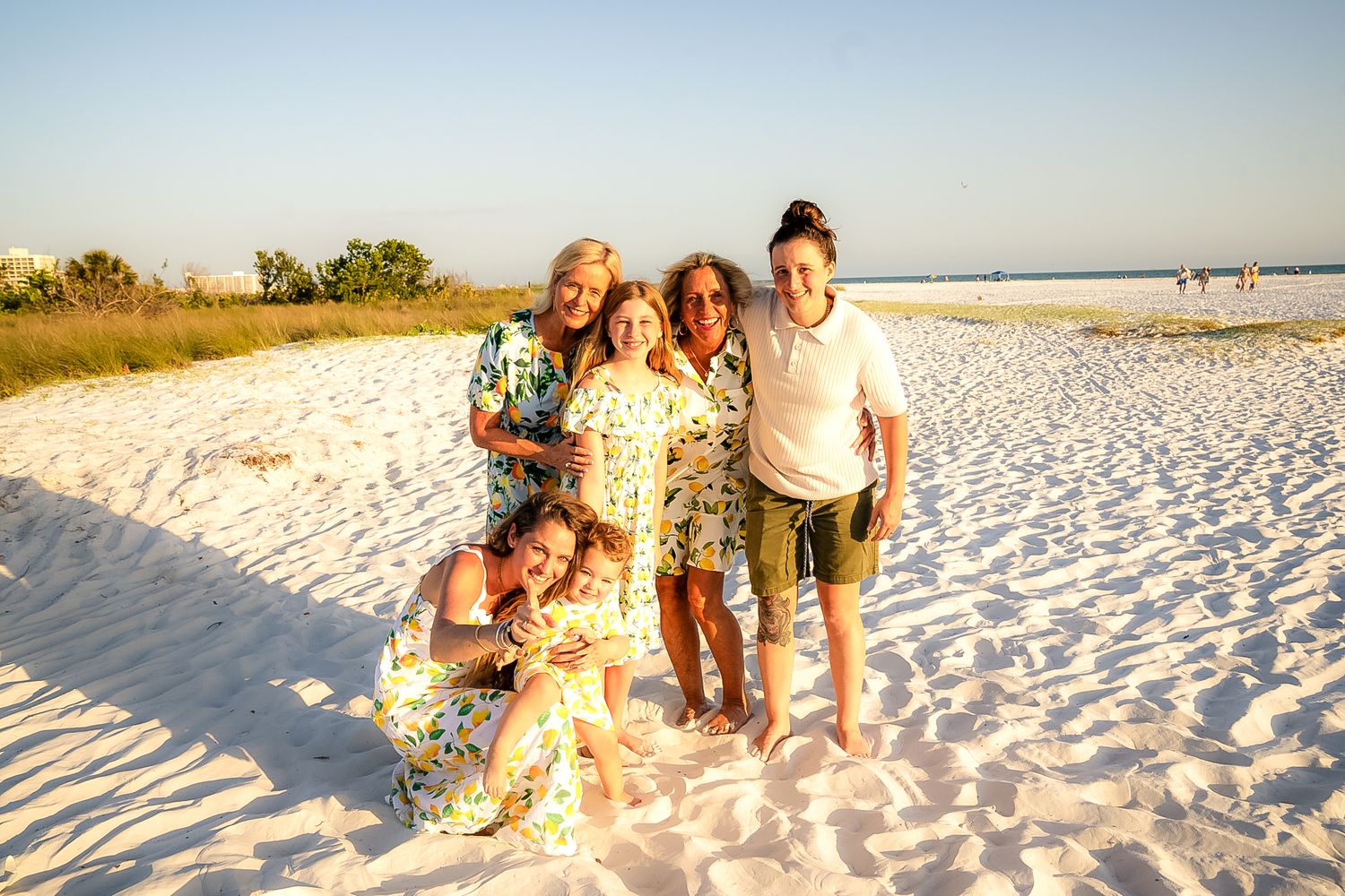 A photo of all the women smiling on the beach with sand and sky.