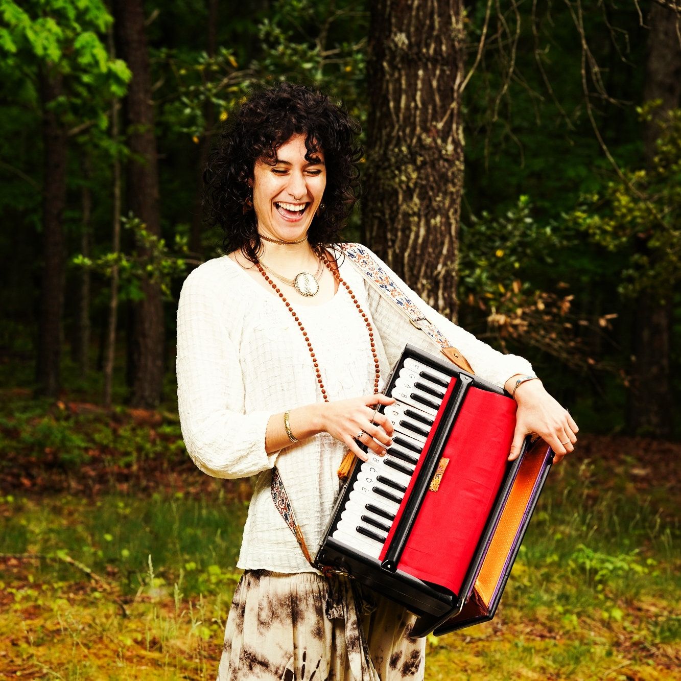 A photo of a woman with black curly hair playing her mini piano that is also red. She is laughing and haveing a good time.
