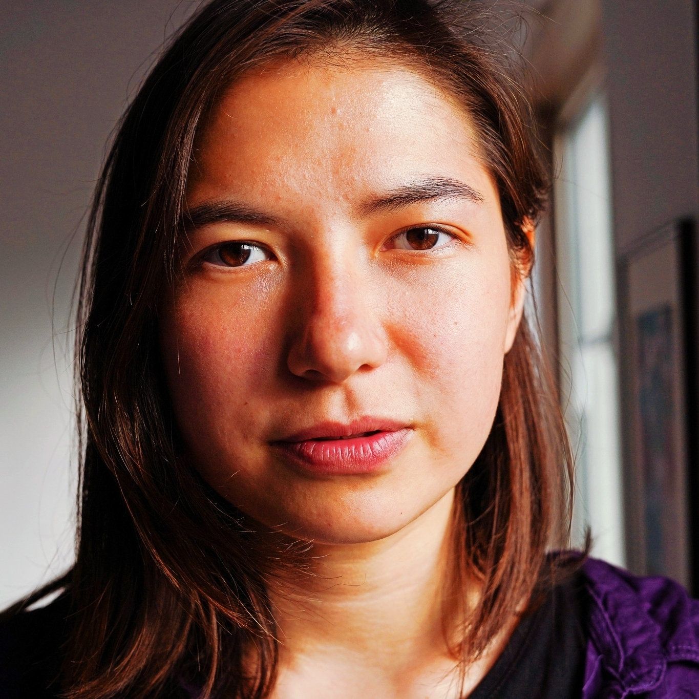 A photo of a woman with brown hair and looking at the camera and wearing a purple shirt.