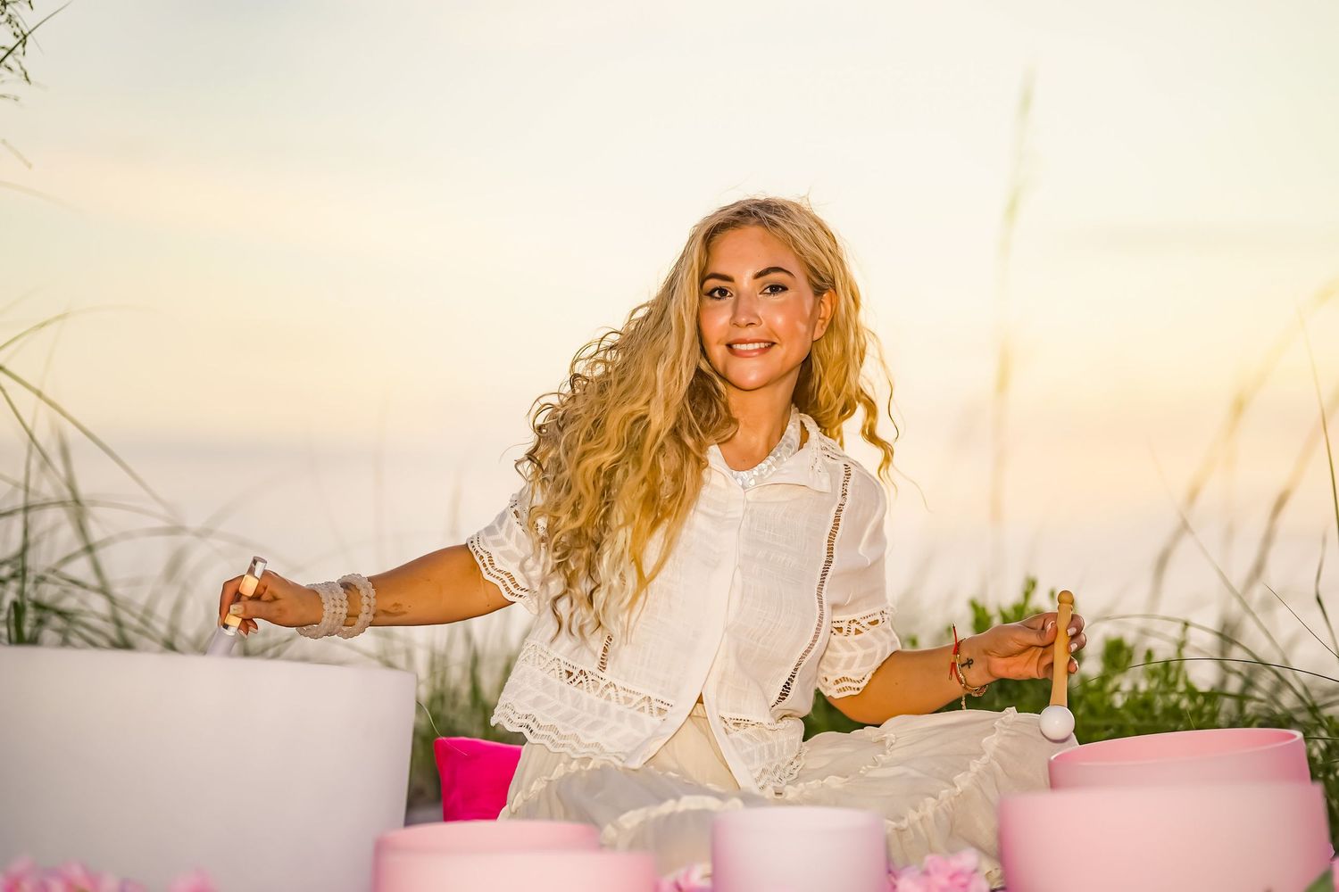 A photo of a blonde woman with flowy and long hair playing the singing bowls.