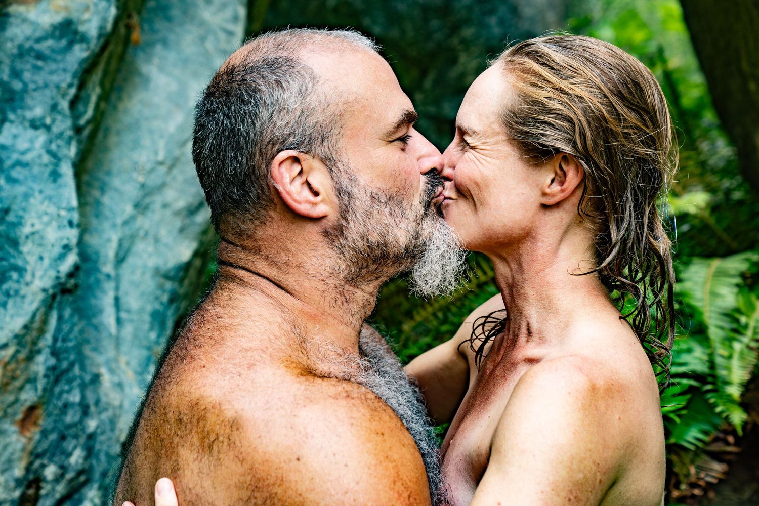Mature couple sharing a romantic moment outdoors, surrounded by lush green foliage and rocky background.