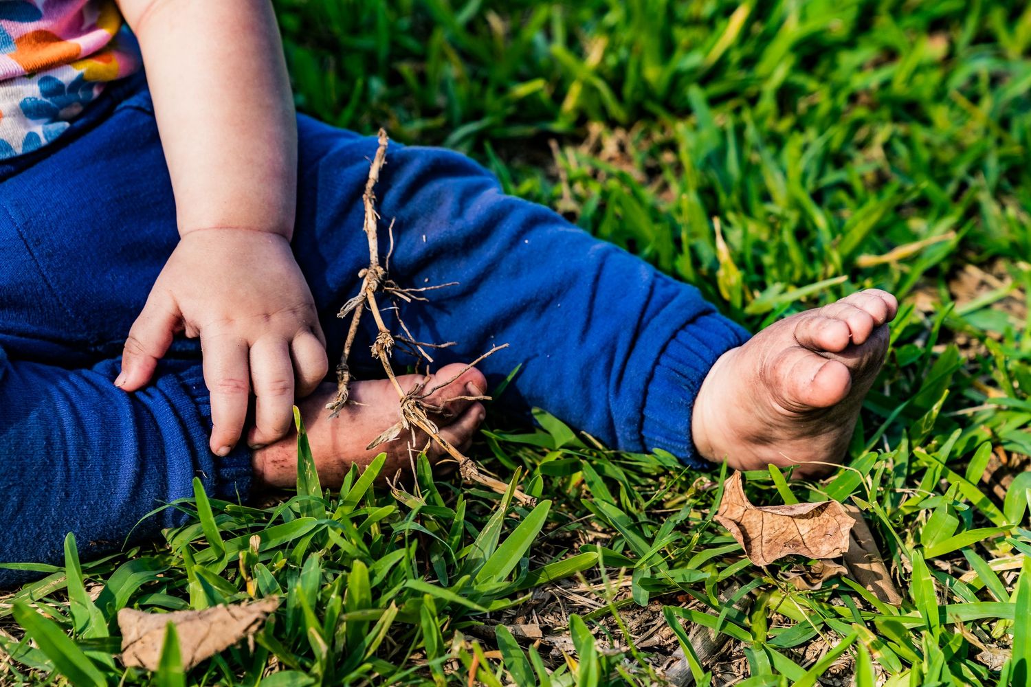 A photo of little girl with little hands and feet resting on the grass wearing blue pants.