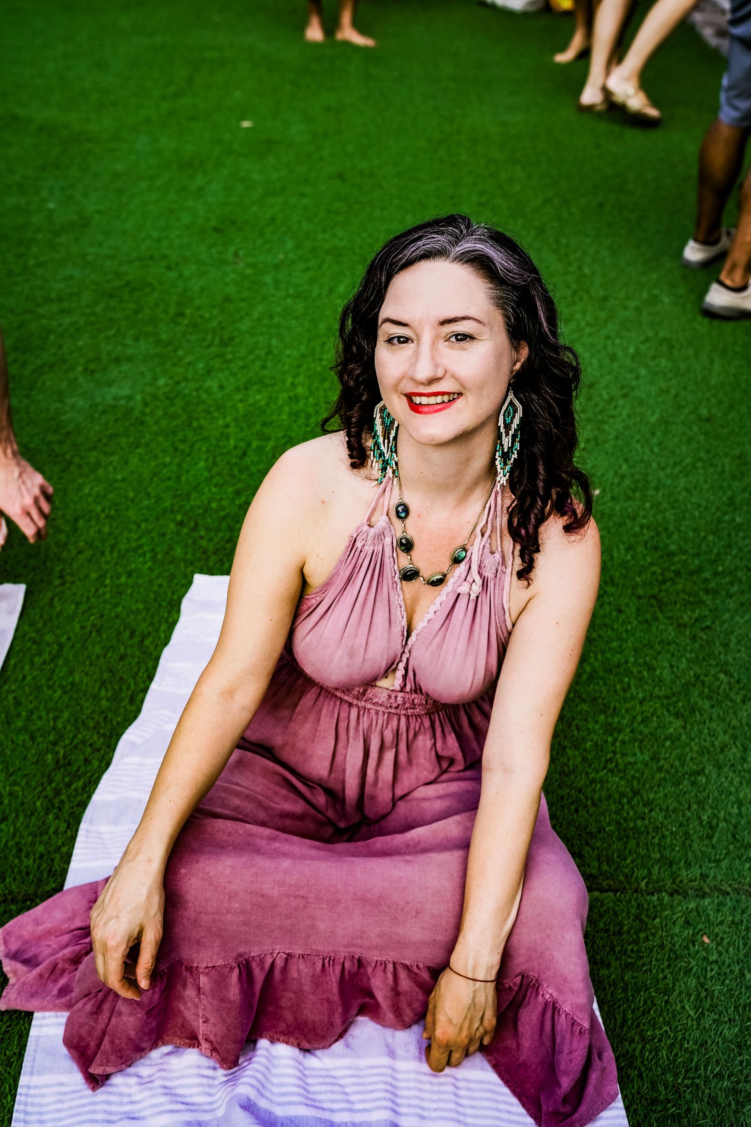 A person in a mauve dress sits on artificial turf in a casual outdoor setting.