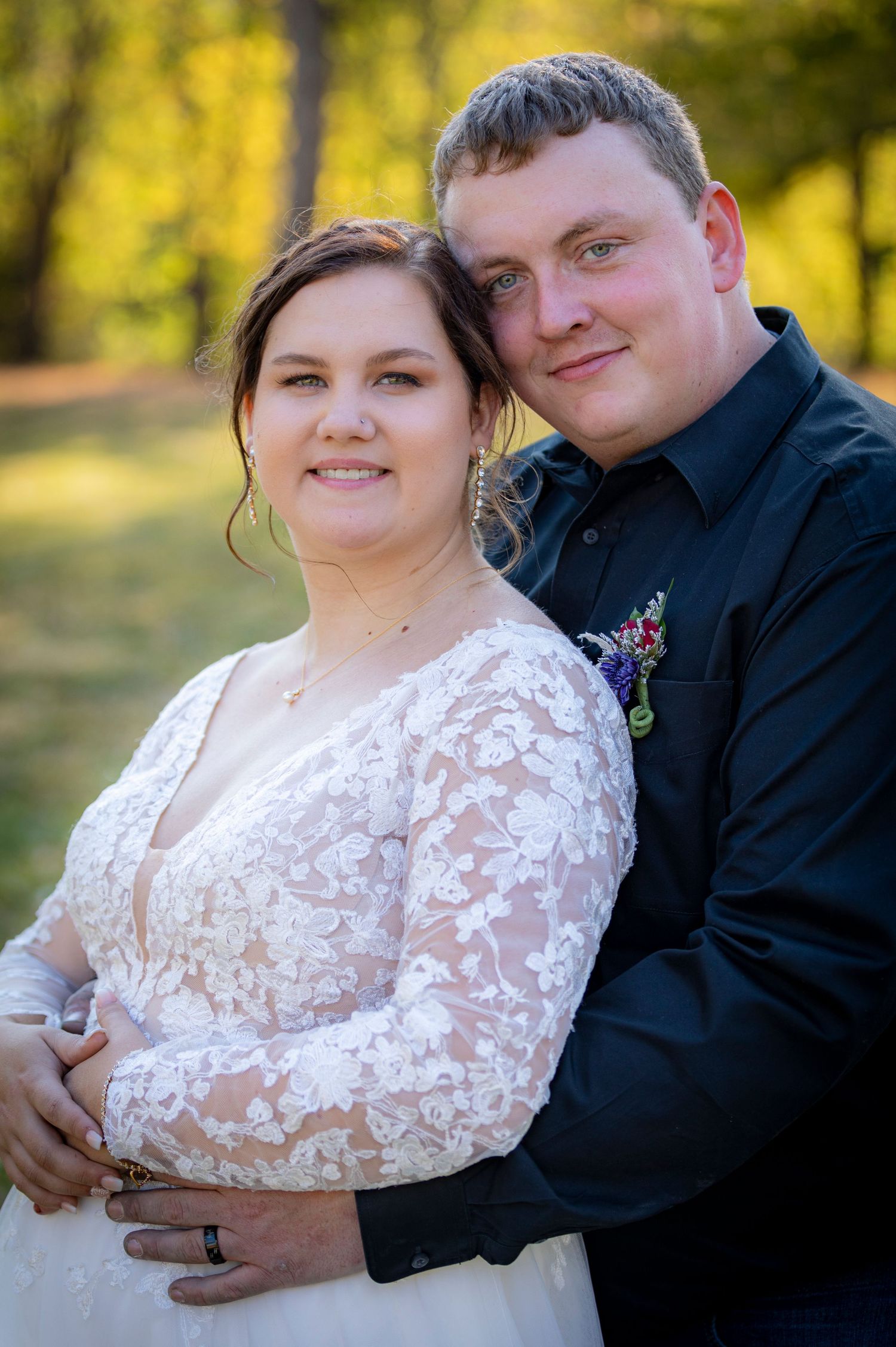 A couple poses outdoors in wedding attire with a beautiful yellow autumn background.