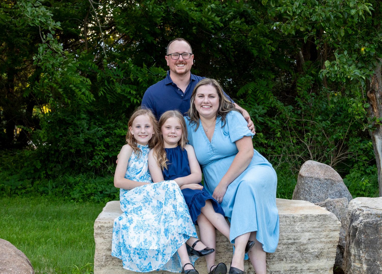 Family members wearing coordinated blue and white outfits pose together on stone steps in an outdoor garden setting.