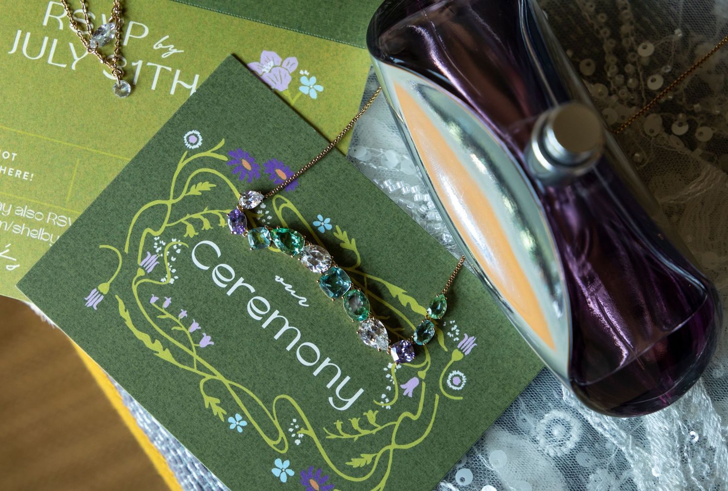 Wedding flat lay including invites, necklace, perfume and laced gloves.