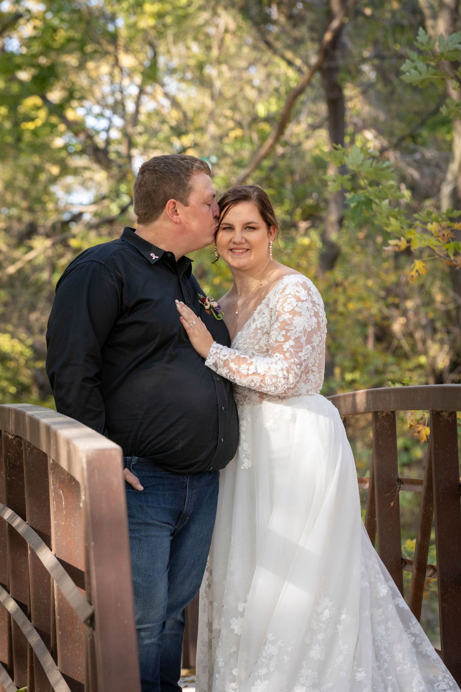 A couple shares a romantic moment on a wooden bridge surrounded by autumn foliage.