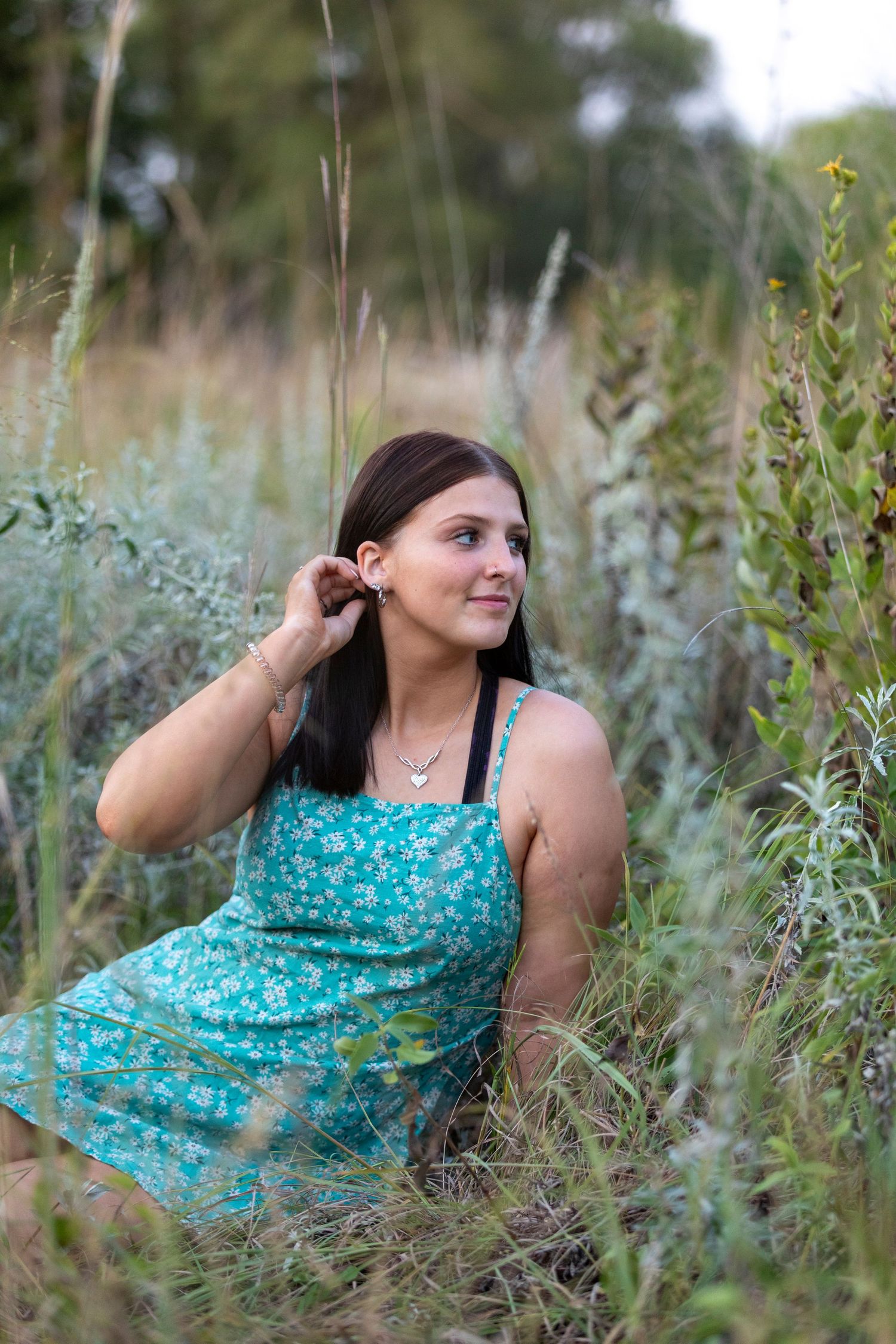 A person in a turquoise dress poses gracefully among tall wildflowers in a natural outdoor setting.