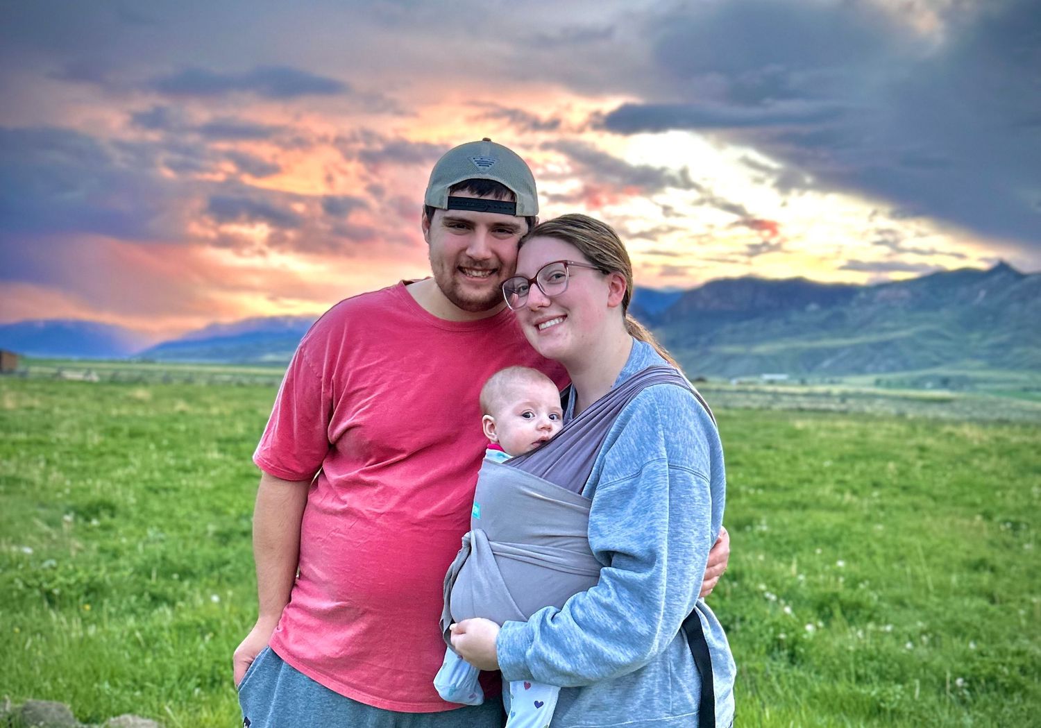 A series of romantic sunset photos showing a couple and baby embracing in a green meadow with mountains in the background.