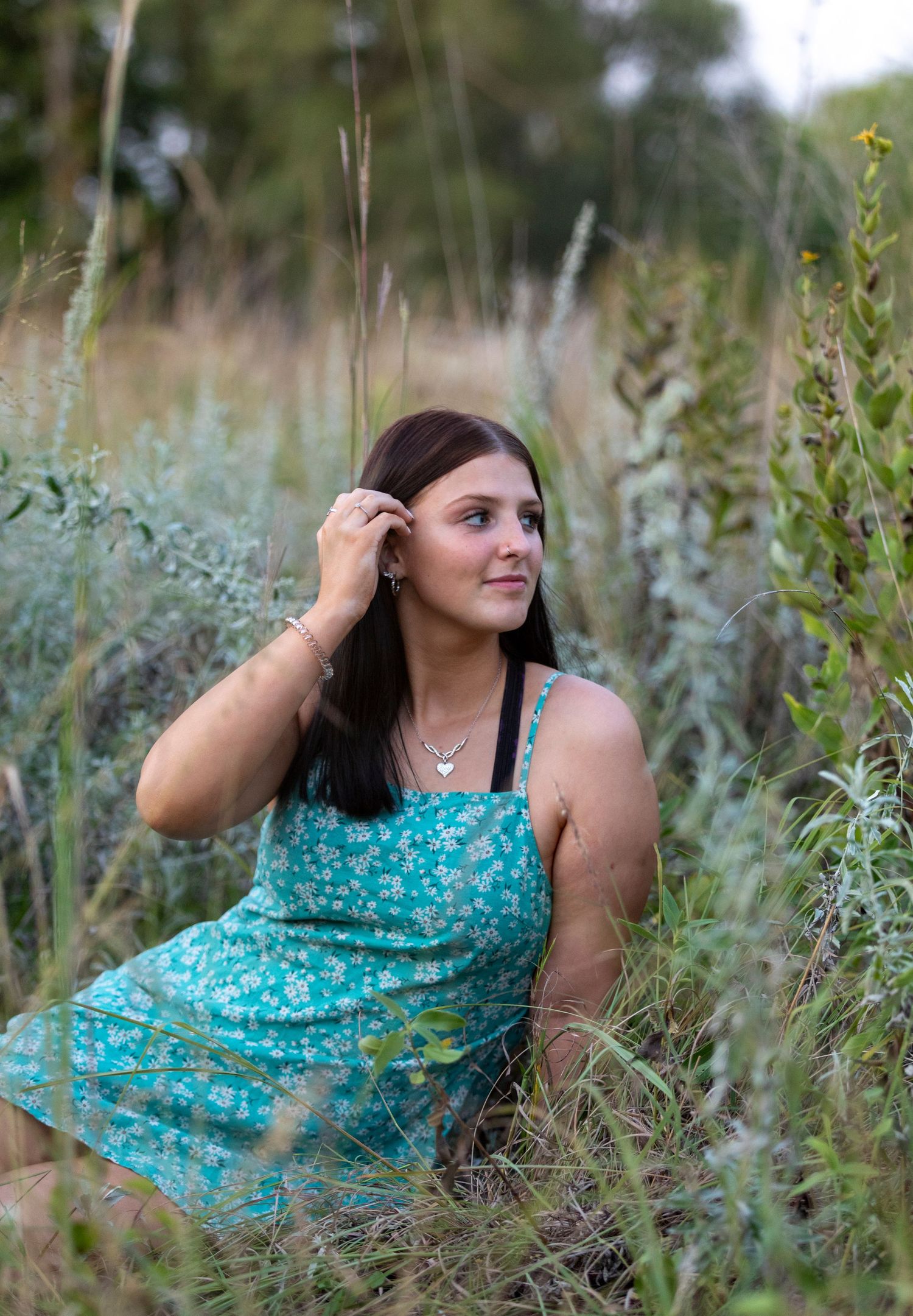 A person in a turquoise floral dress poses gracefully among tall wildflowers and grasses in a natural outdoor setting.