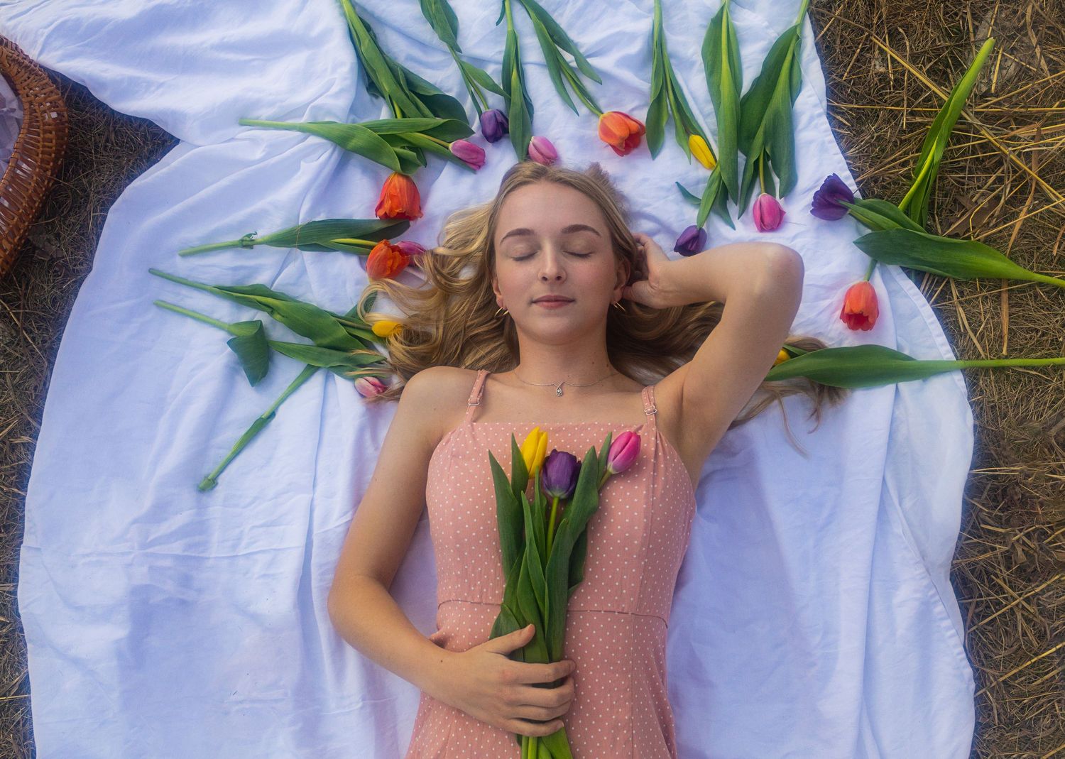 Person lying on white fabric outdoors holds colorful tulips while posing for artistic spring photography.