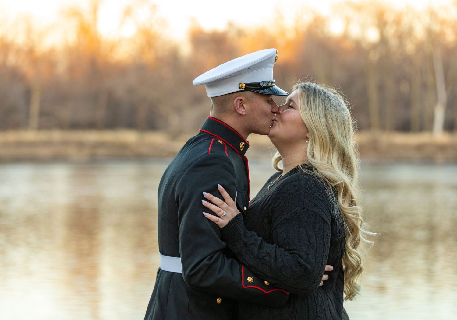 A couple in marine dress uniform shares romantic moments by a lake during sunset.