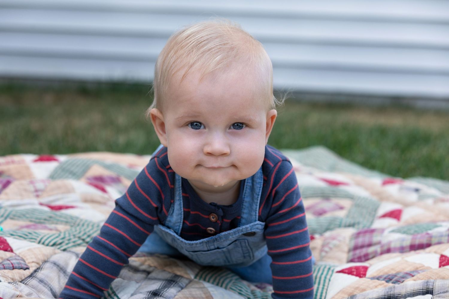 A small child in a striped shirt lies on a colorful patchwork quilt outdoors.