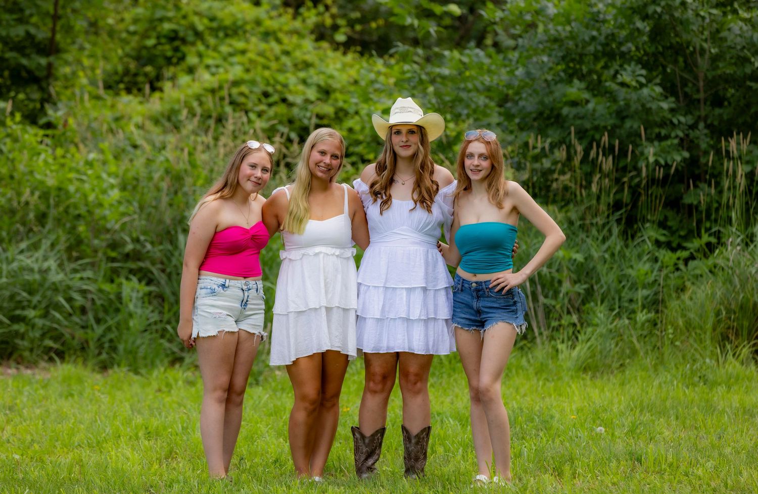 A group of people pose together on grassy terrain in casual summer outfits during a sunny day.