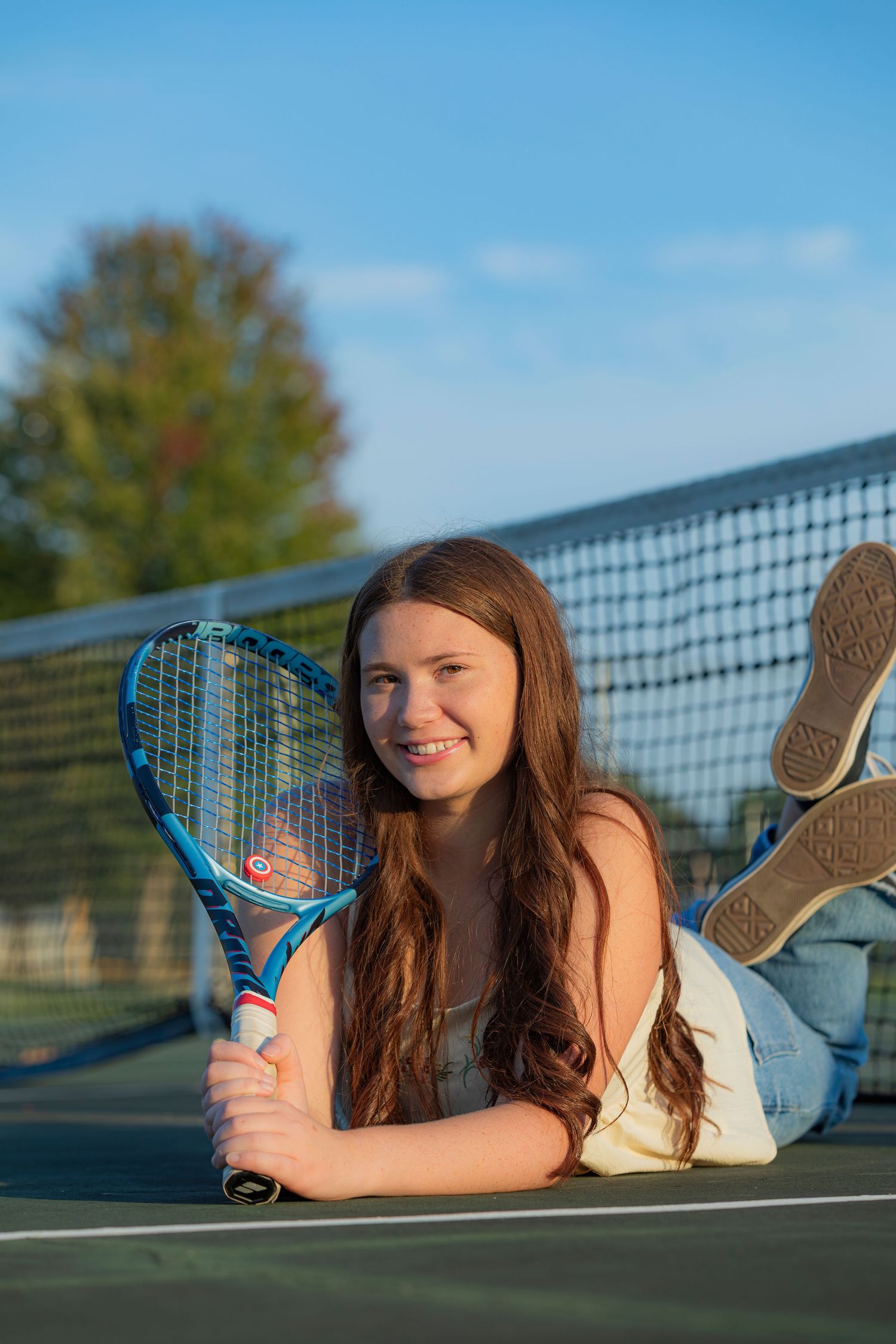 Tennis player lying on court with blue racket posing for creative senior photography series.