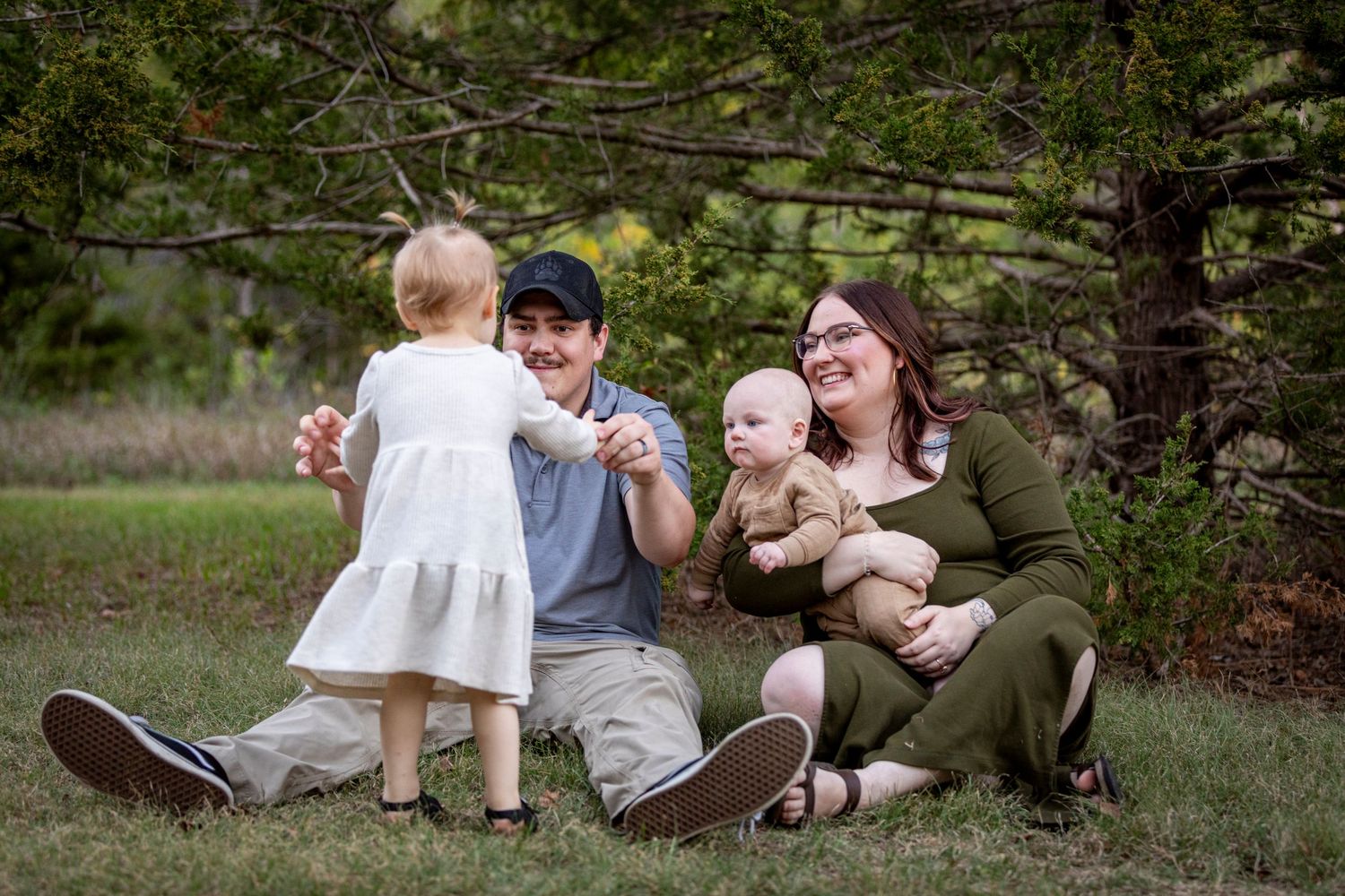 A family sits together on grass in a park during an outdoor photo session, creating candid moments in nature.