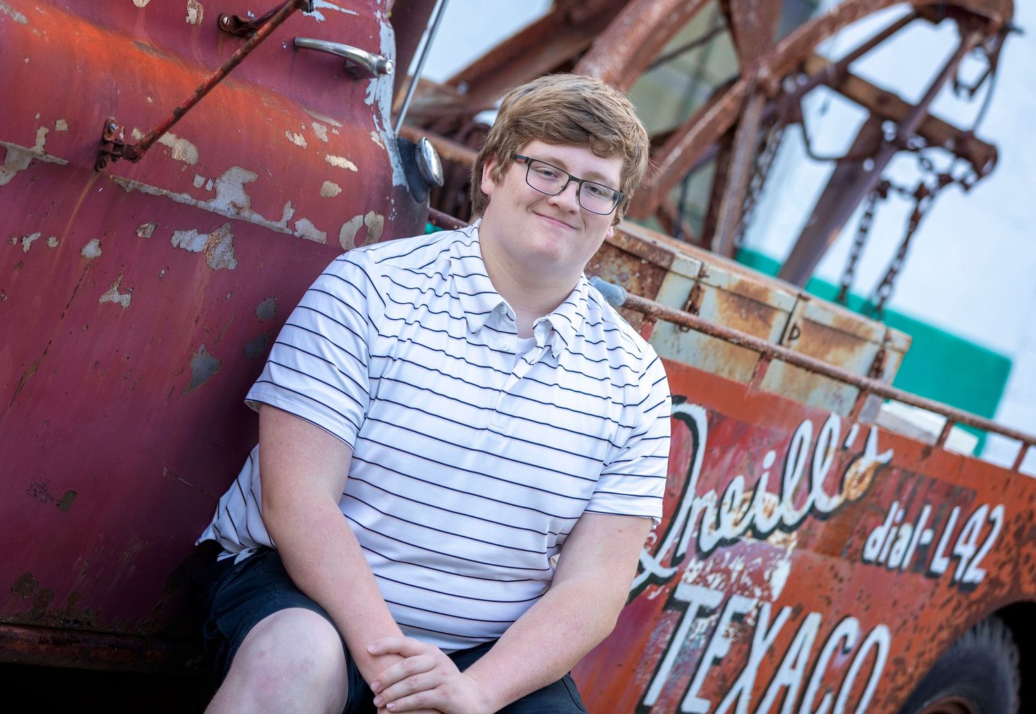 A person in a striped shirt sits outdoors near a vintage Texaco gas station sign.