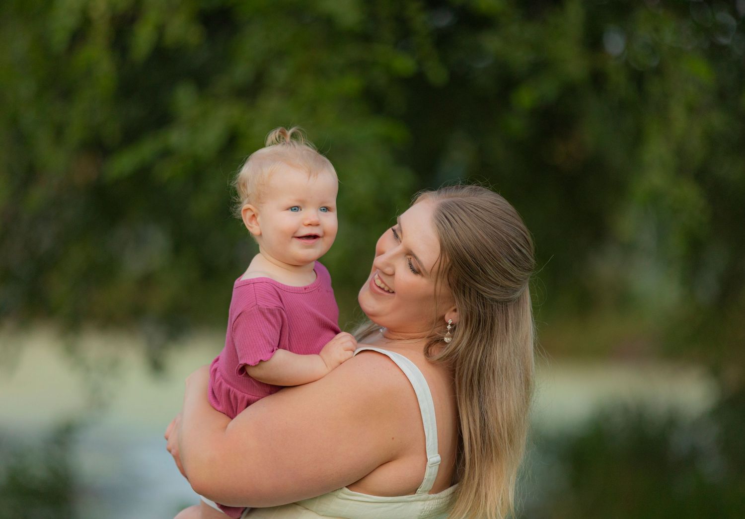 A tender moment between parent and child outdoors with soft natural lighting and greenery in the background.