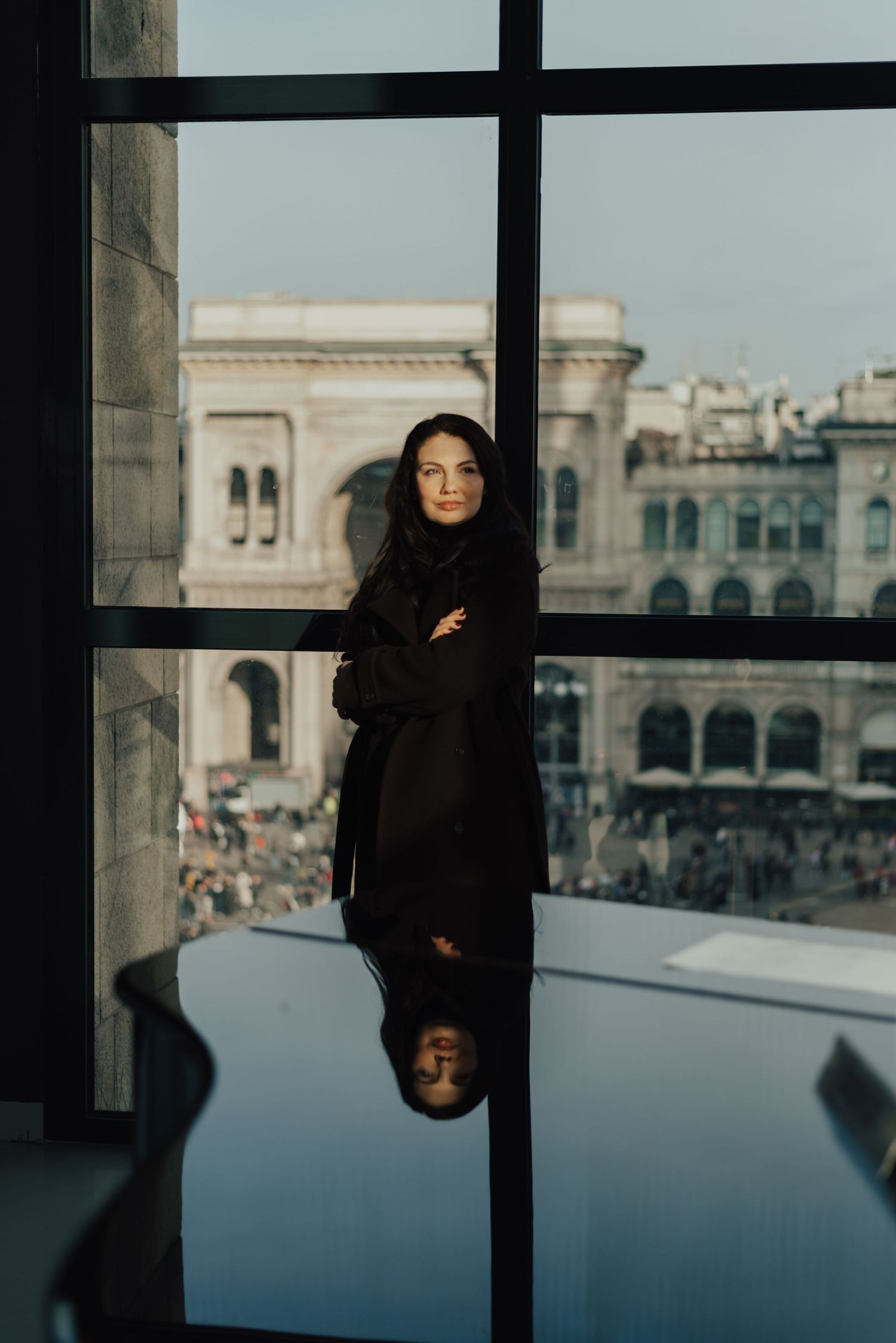 A series of moody window portraits showing a figure in black against an urban backdrop with architectural details.