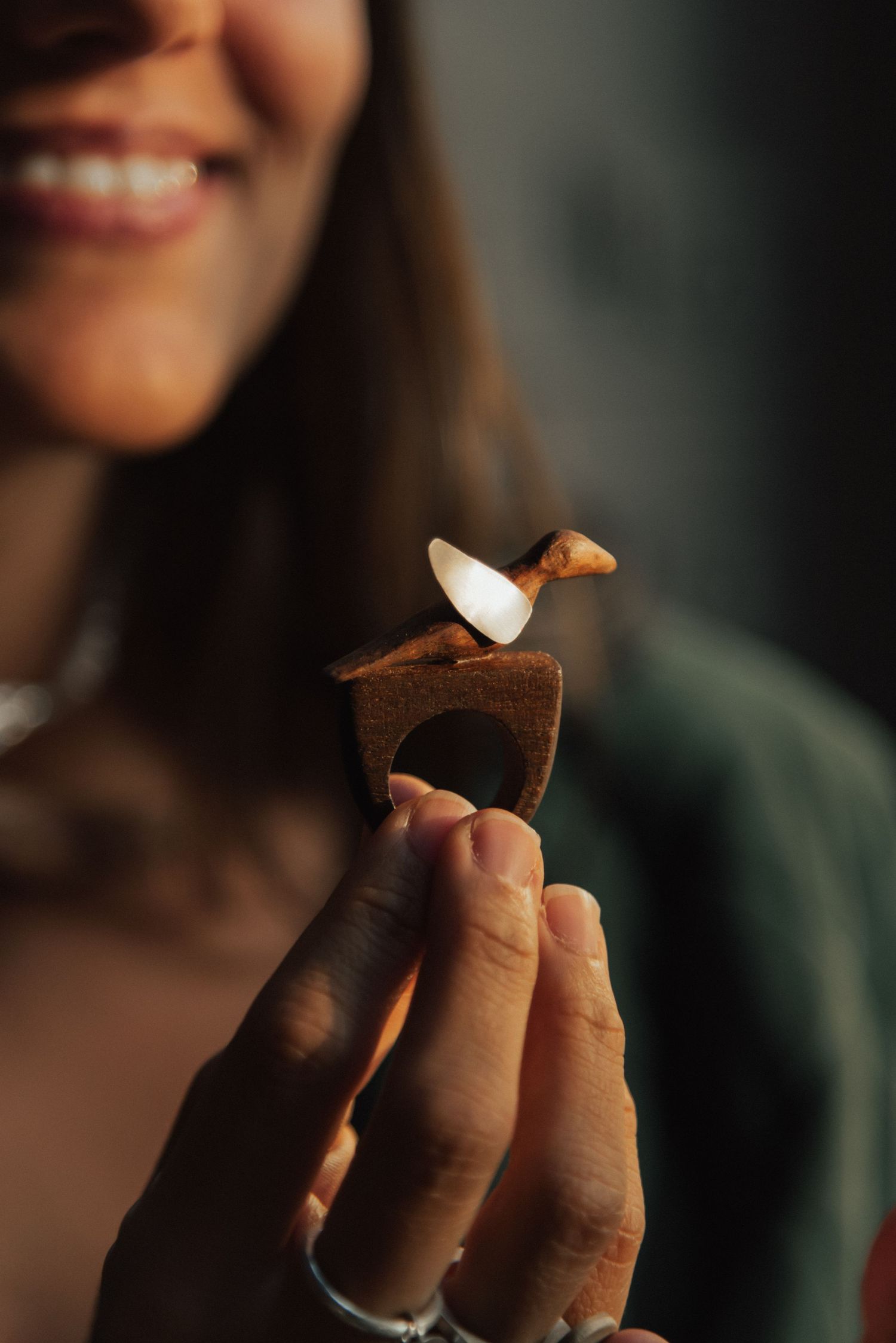Person breaks apart a dark chocolate cookie while smiling in a dimly lit setting.