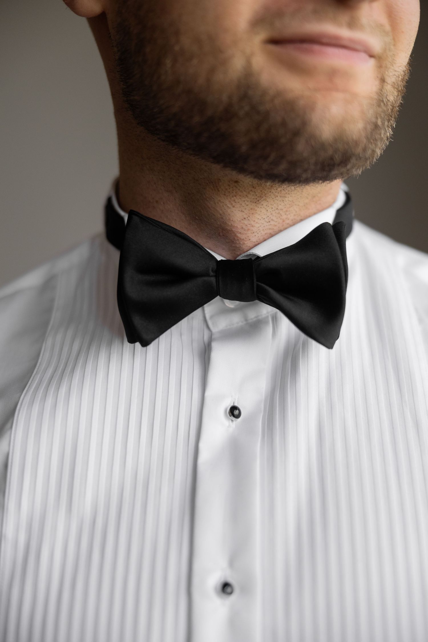 Man in white tuxedo shirt and black bow tie, close-up formal wedding attire.