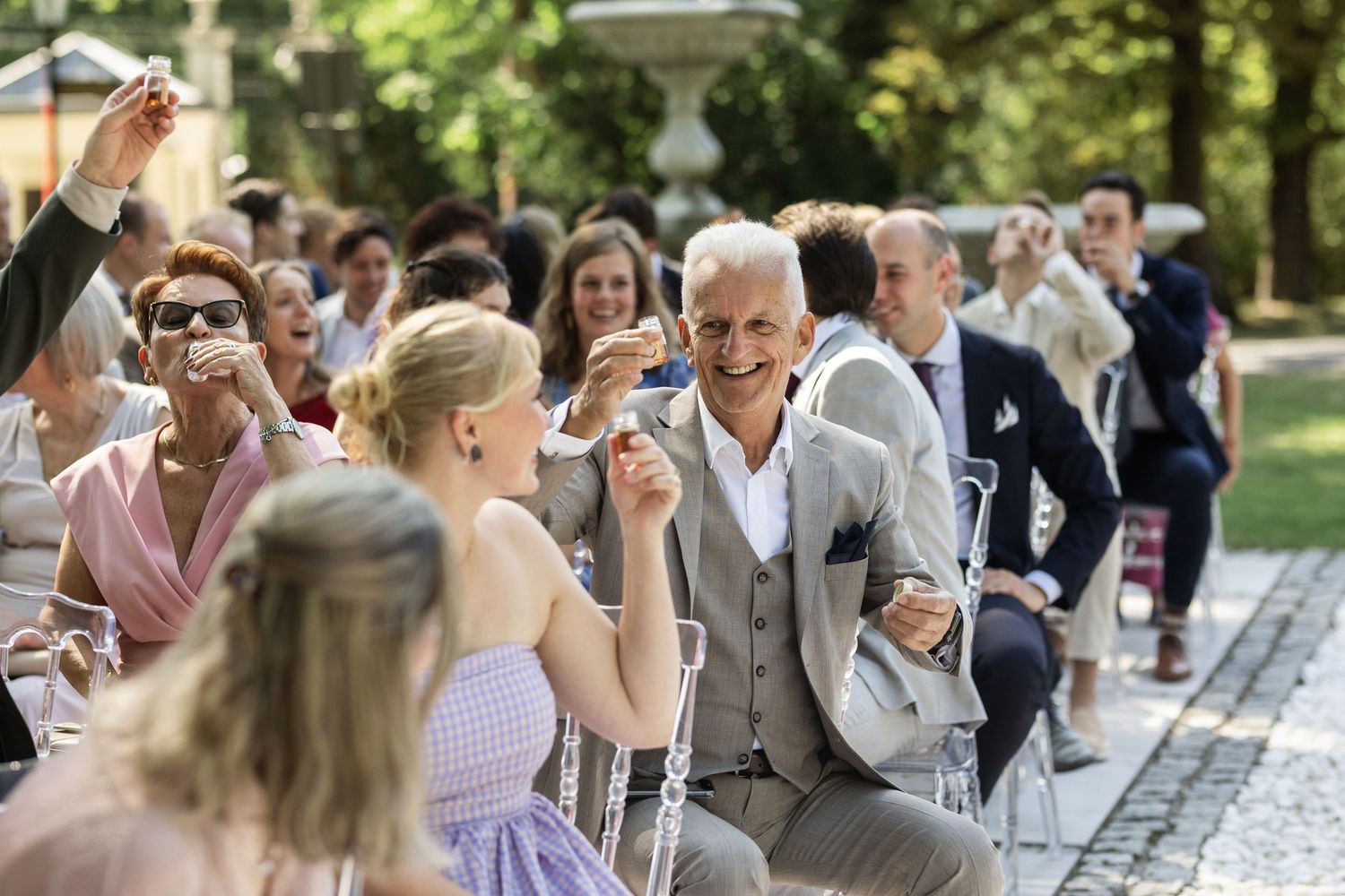 Wedding guests seated at outdoor tables enjoy a celebratory meal in a garden setting.