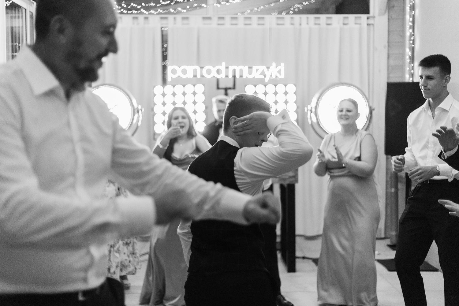 Black and white photo of people dancing and socializing at an indoor celebration event with decorative lighting.