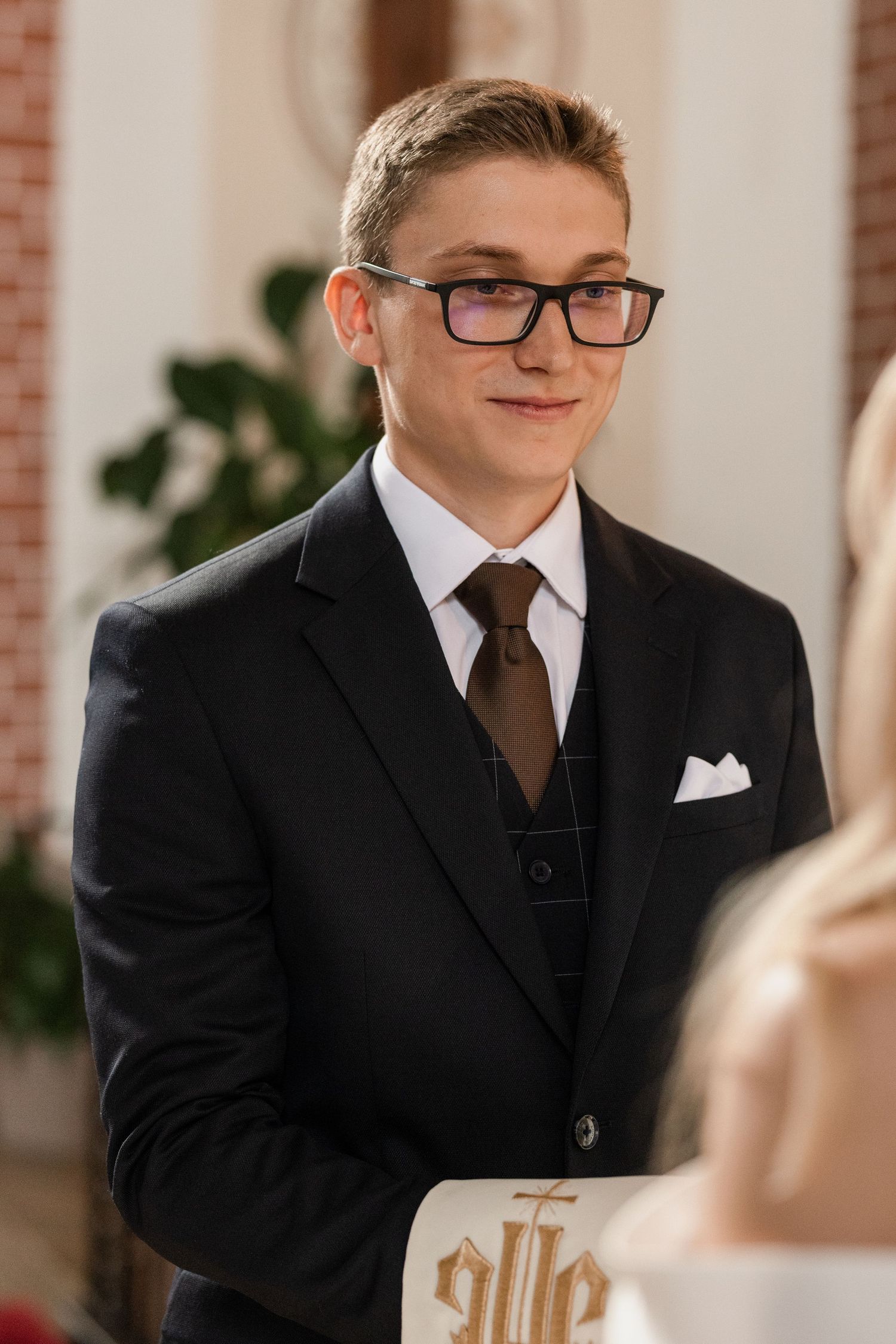 A young person in a formal black suit and glasses poses for a series of portrait shots.