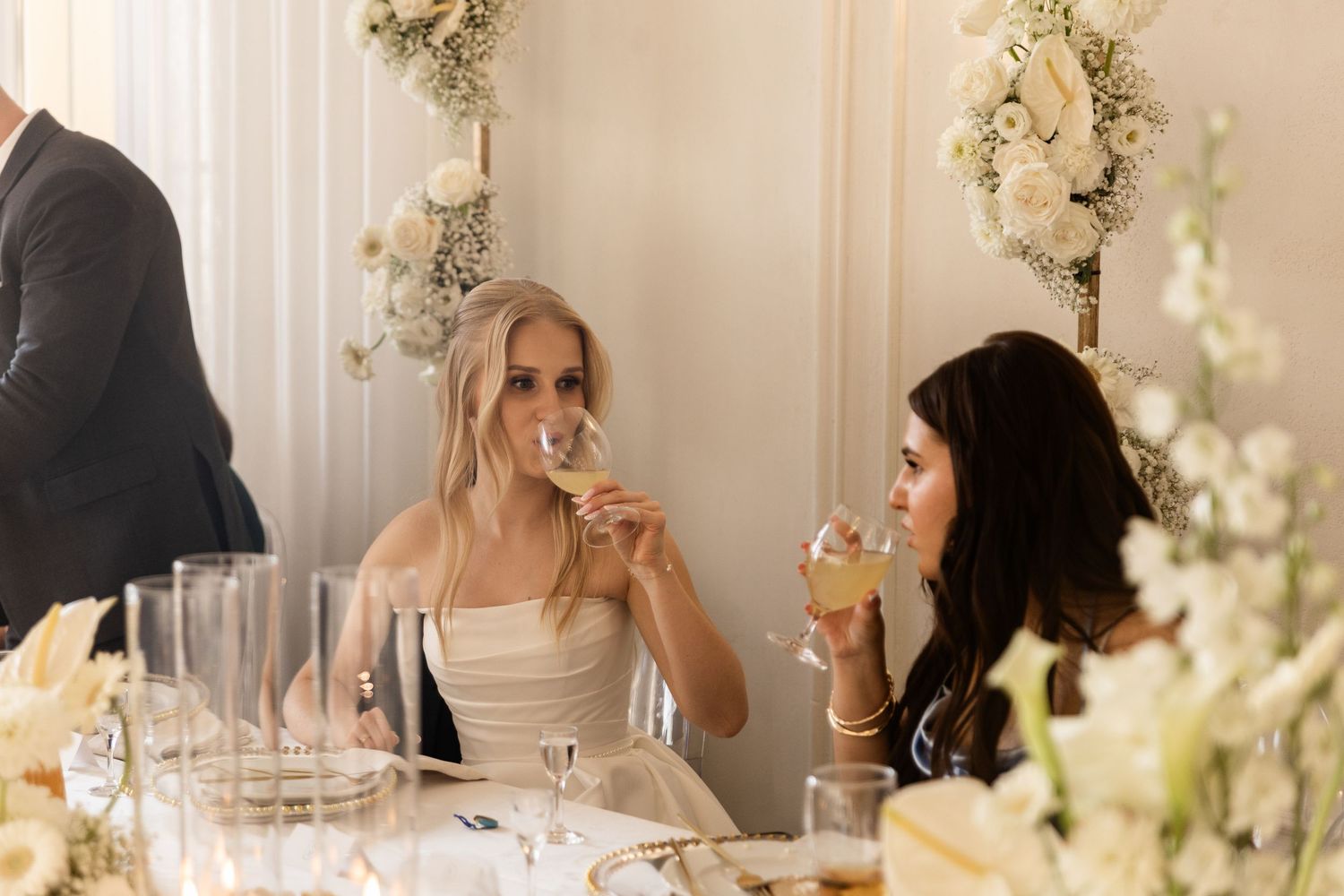 A couple sits together at an elegant wedding reception table decorated with white floral centerpieces and candles.