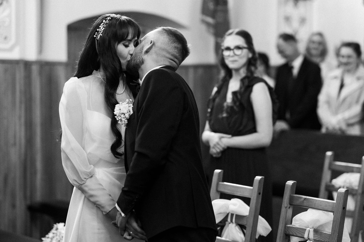 A couple shares their first kiss during a wedding ceremony as guests look on with smiles in the background.