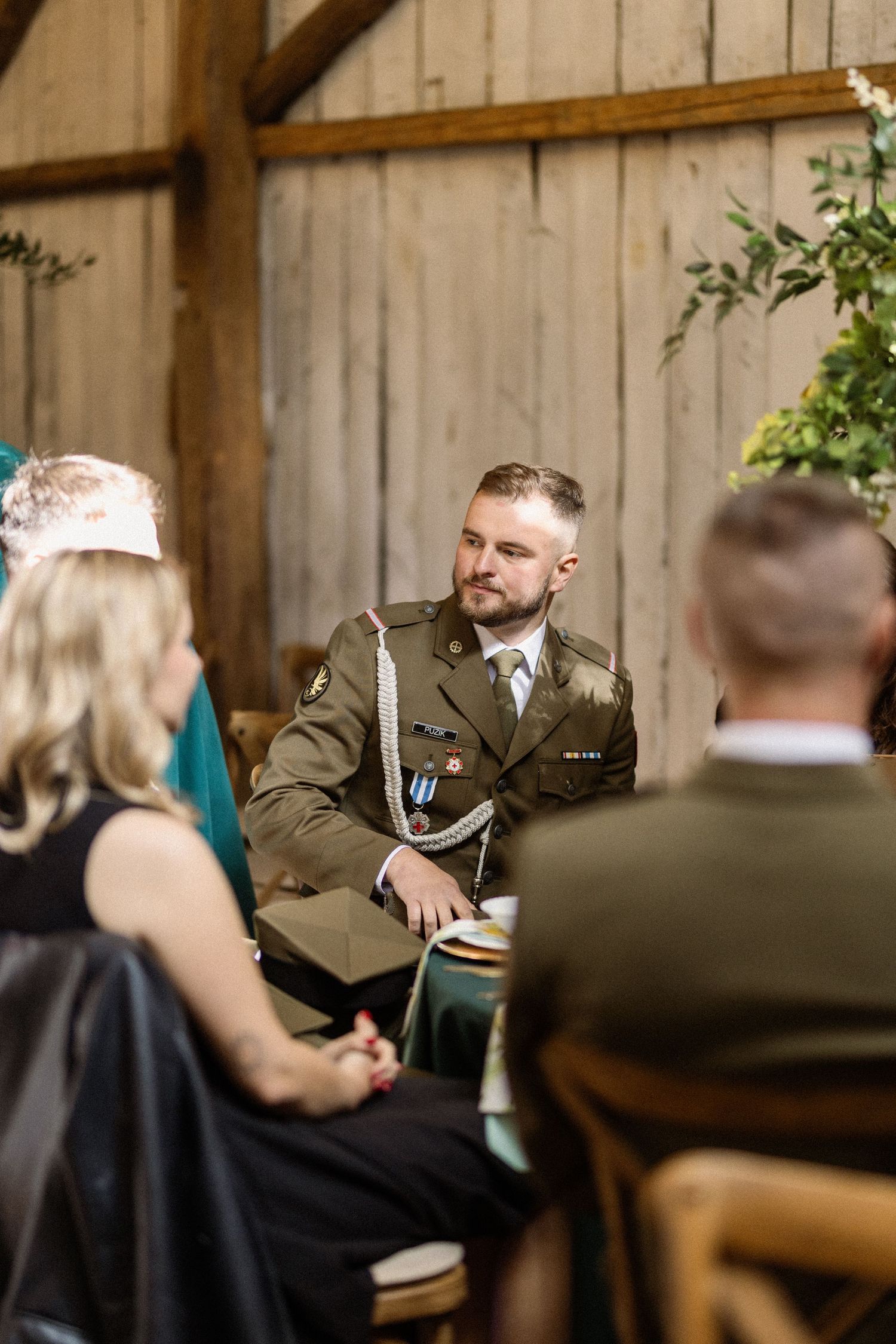 People in formal attire having a conversation inside a rustic wooden barn setting.