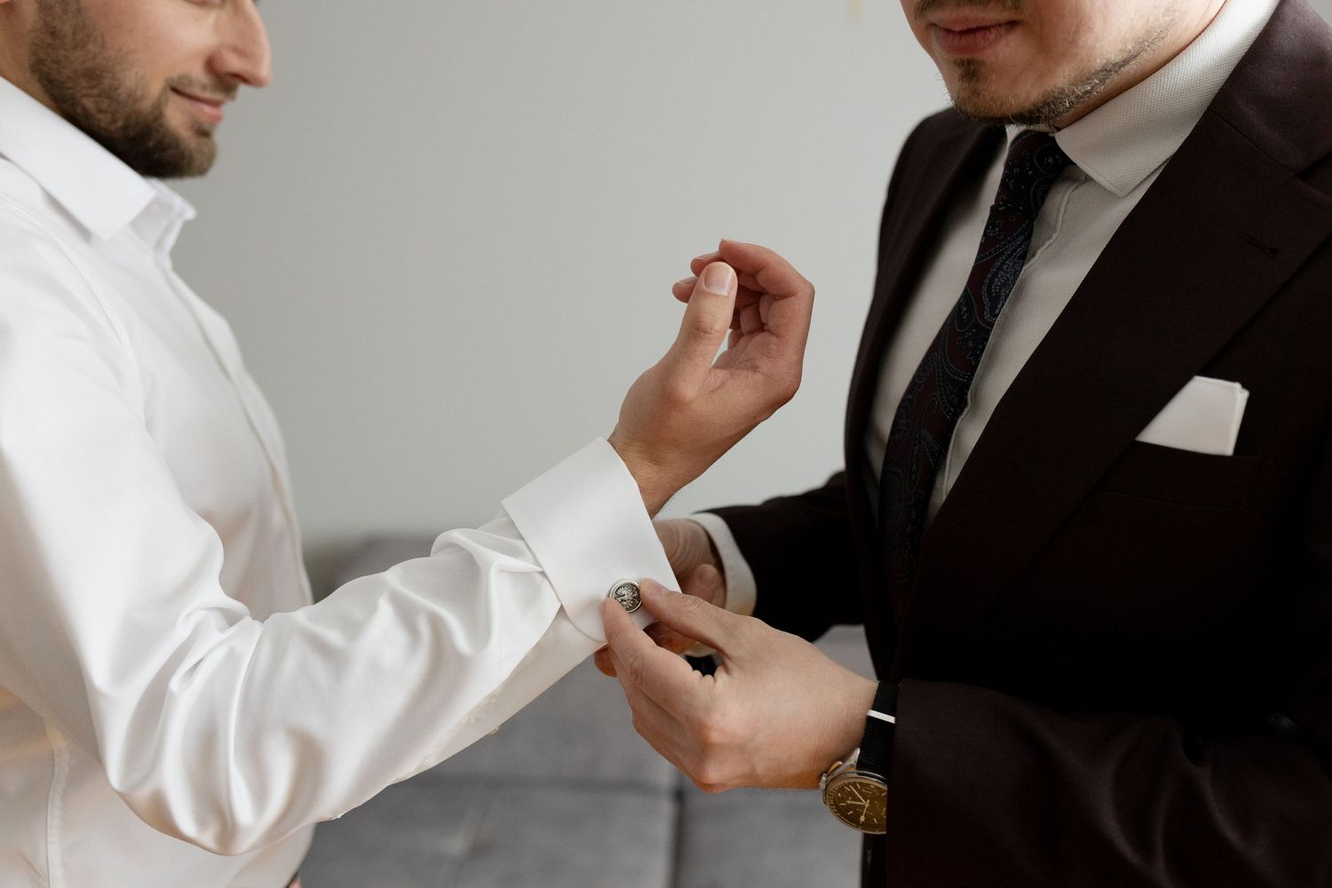 Someone helping adjust the cuff of a white dress shirt while wearing a black suit and pocket square.