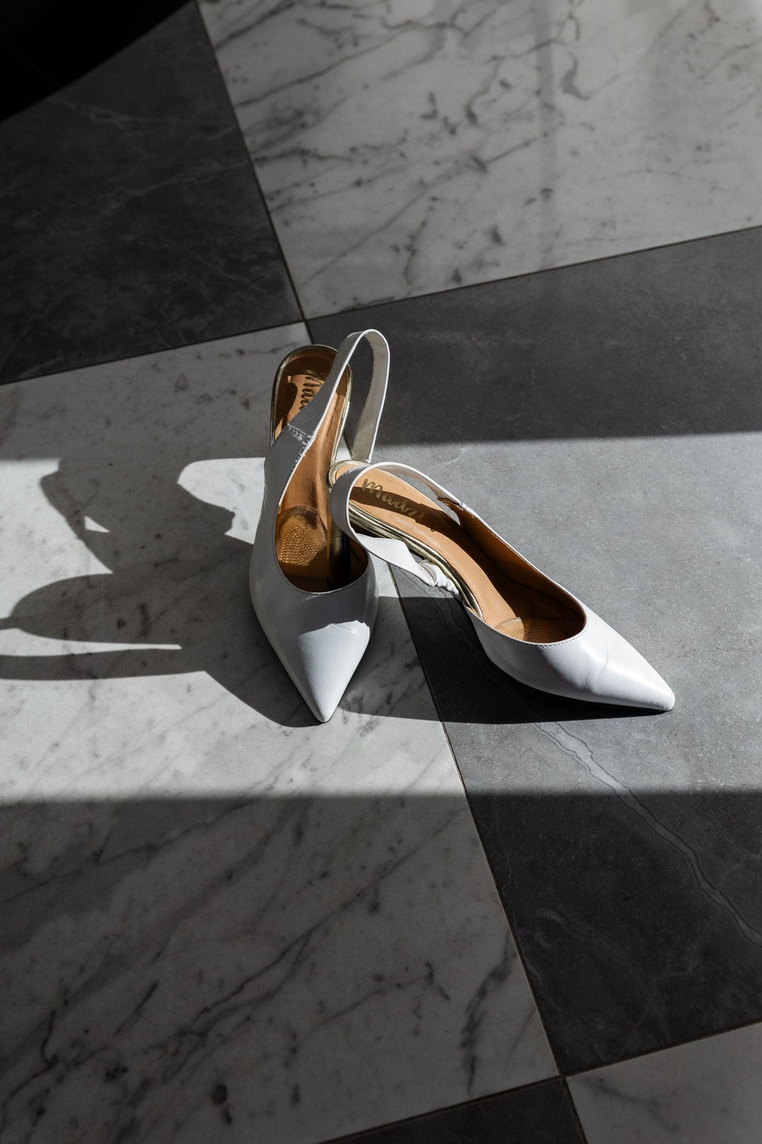 White leather slingback kitten heels on contrasting black and white marble floor with dramatic shadows.