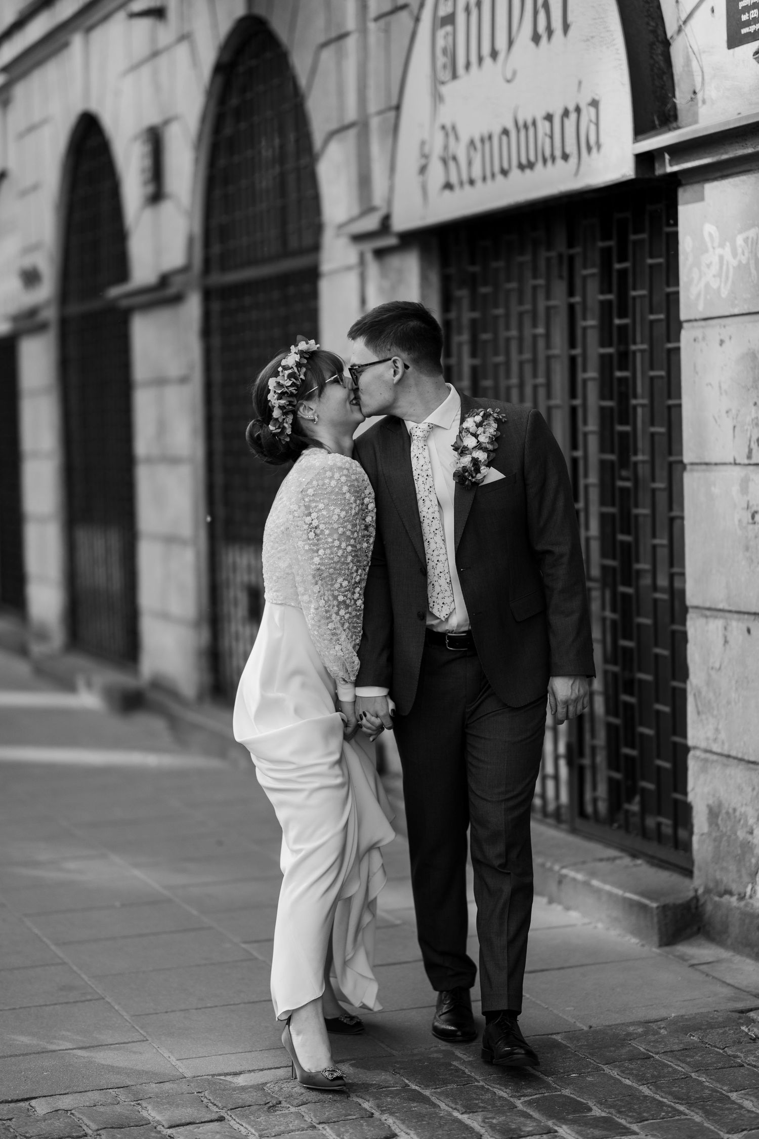 A black and white romantic wedding photograph showing a couple sharing a kiss on a cobblestone street in front of an old building.