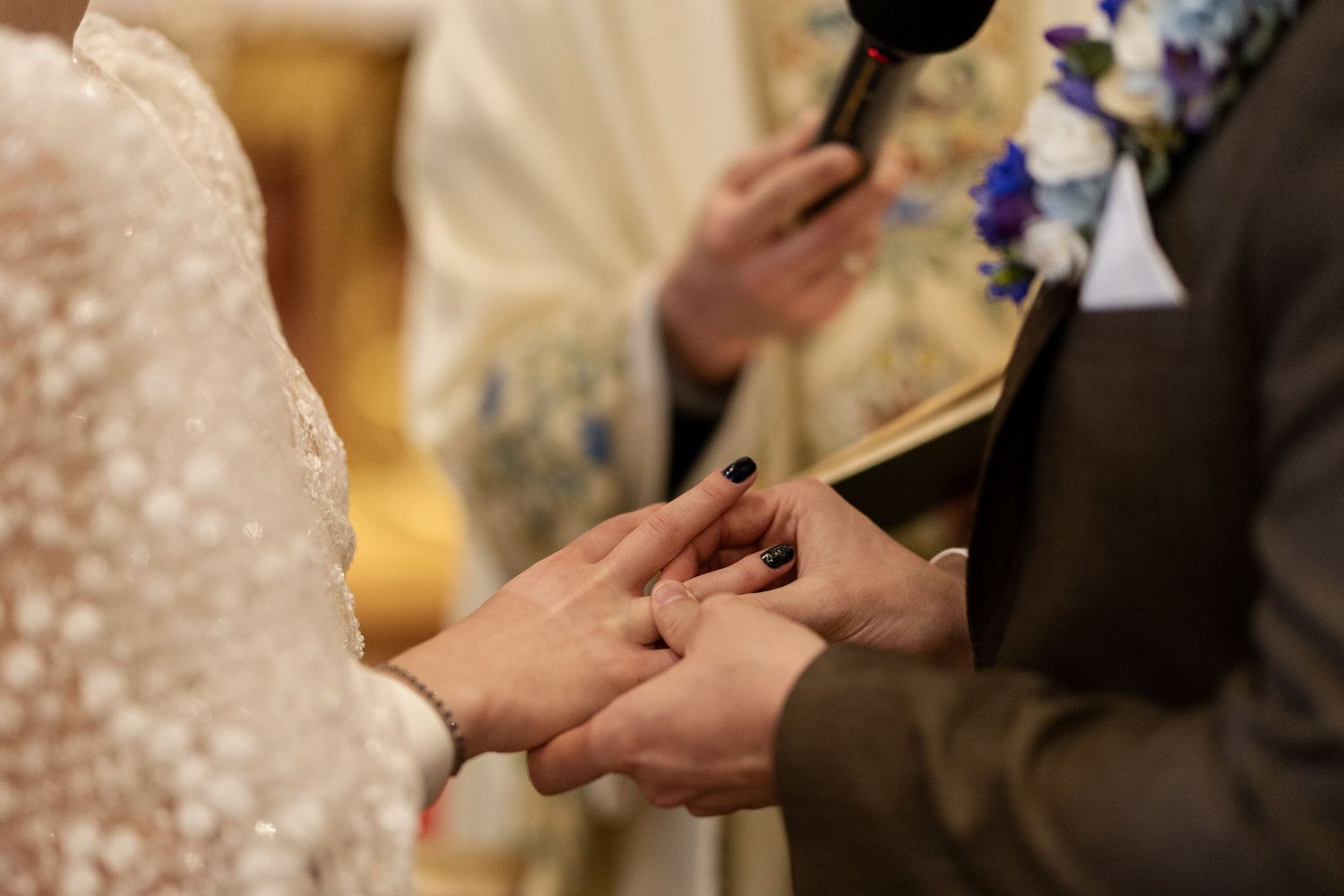 A close-up of hands exchanging rings during a traditional wedding ceremony, with delicate lace visible in the frame.
