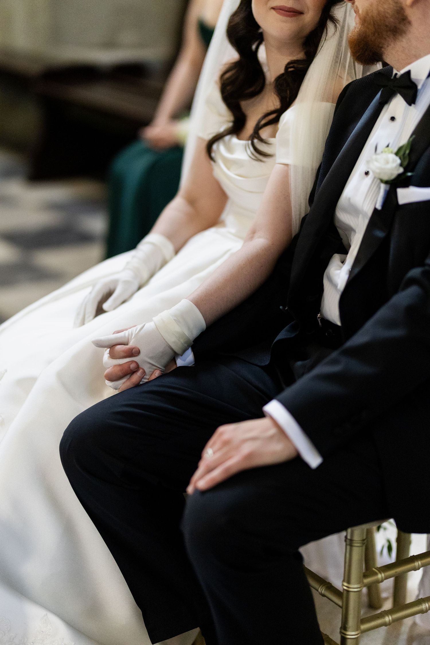 Close-up of newlyweds seated together showing bride in white gown with long gloves and groom in classic tuxedo.