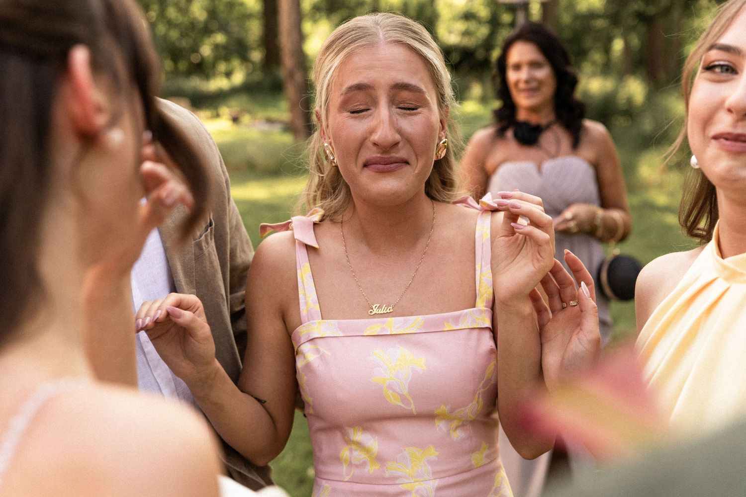 A group of wedding guests enjoy a candid moment together outdoors in natural lighting.