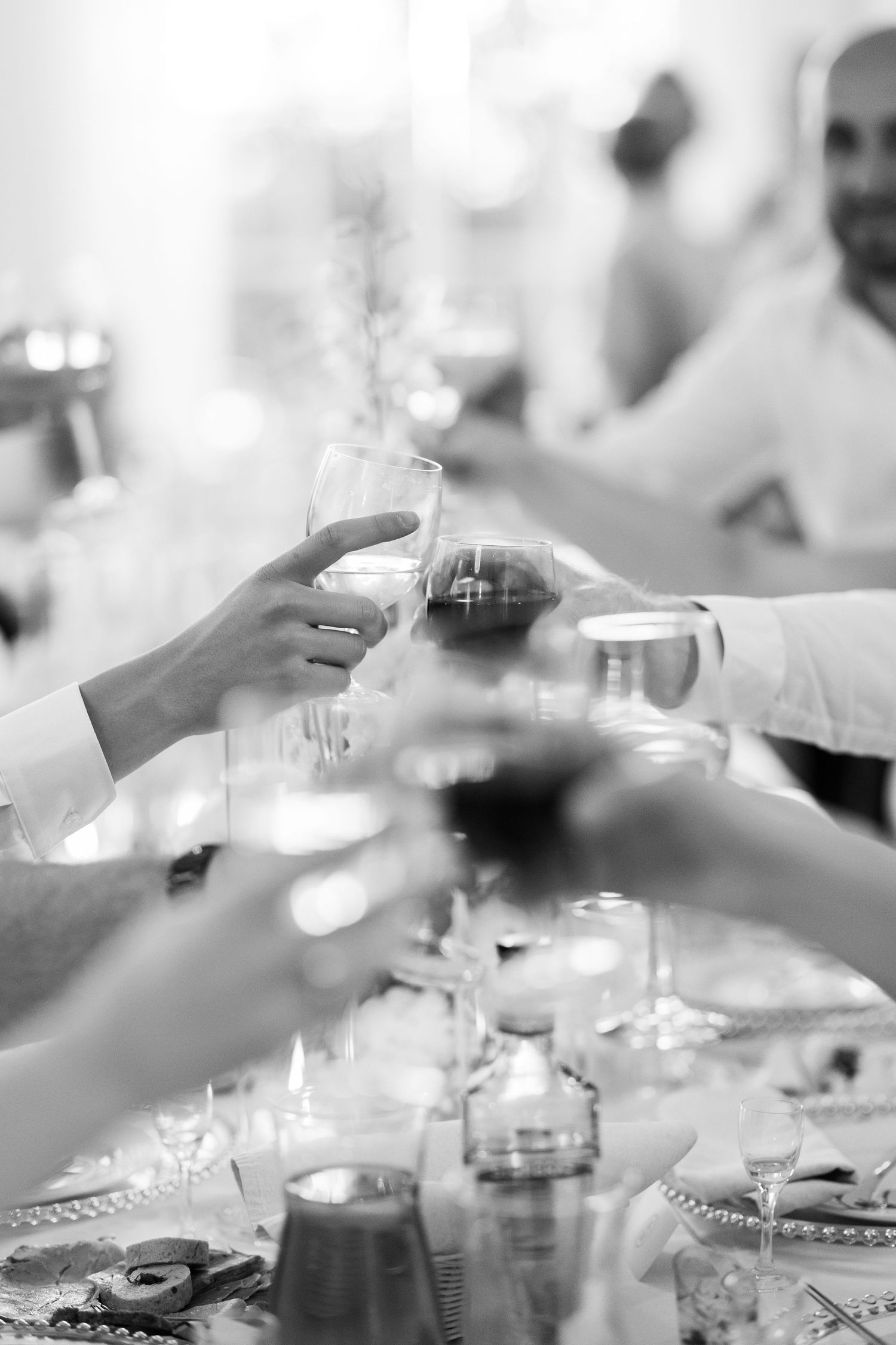 Multiple hands clink glasses together over a formal dining table in a monochromatic celebration scene.